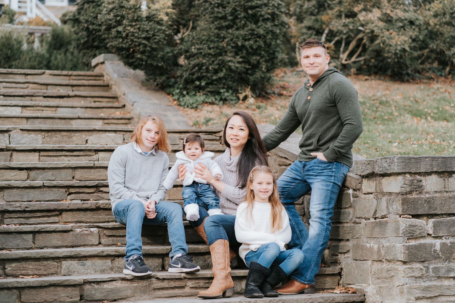 Family portrait on rustic stone steps with natural greenery background.