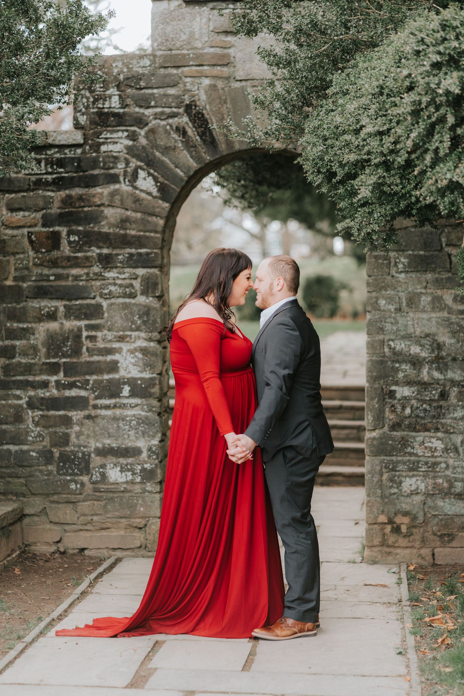 A couple in formal attire shares a romantic moment under a stone archway.
