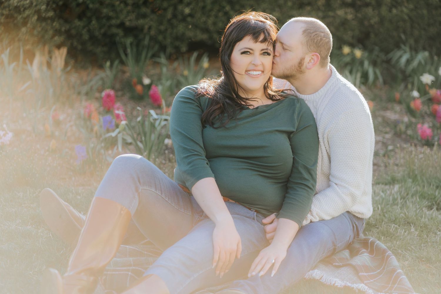 A couple shares a tender moment while sitting among blooming flowers in a garden.