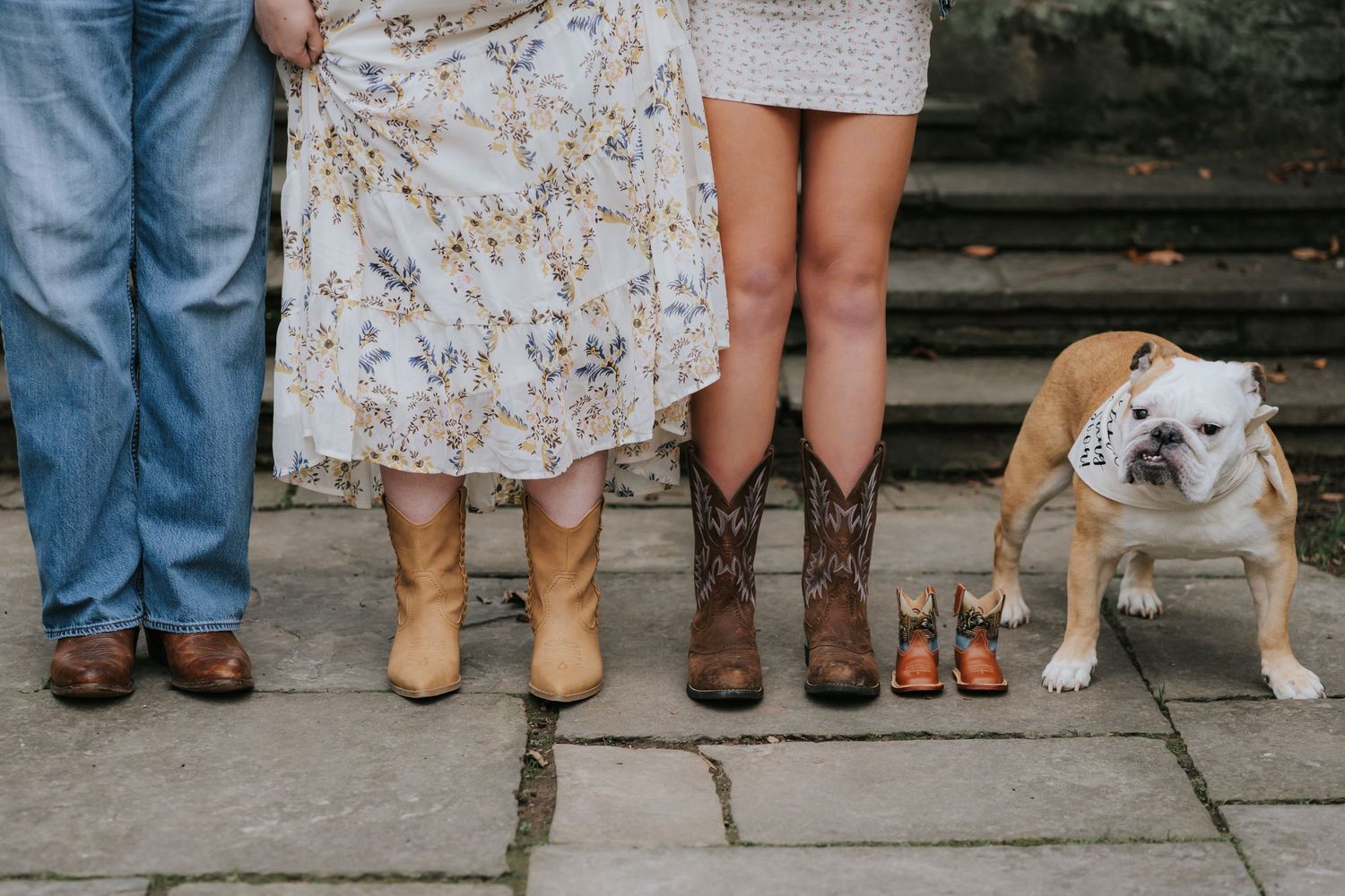 Cropped view of legs and feet with a bulldog sitting beside them on stone steps.