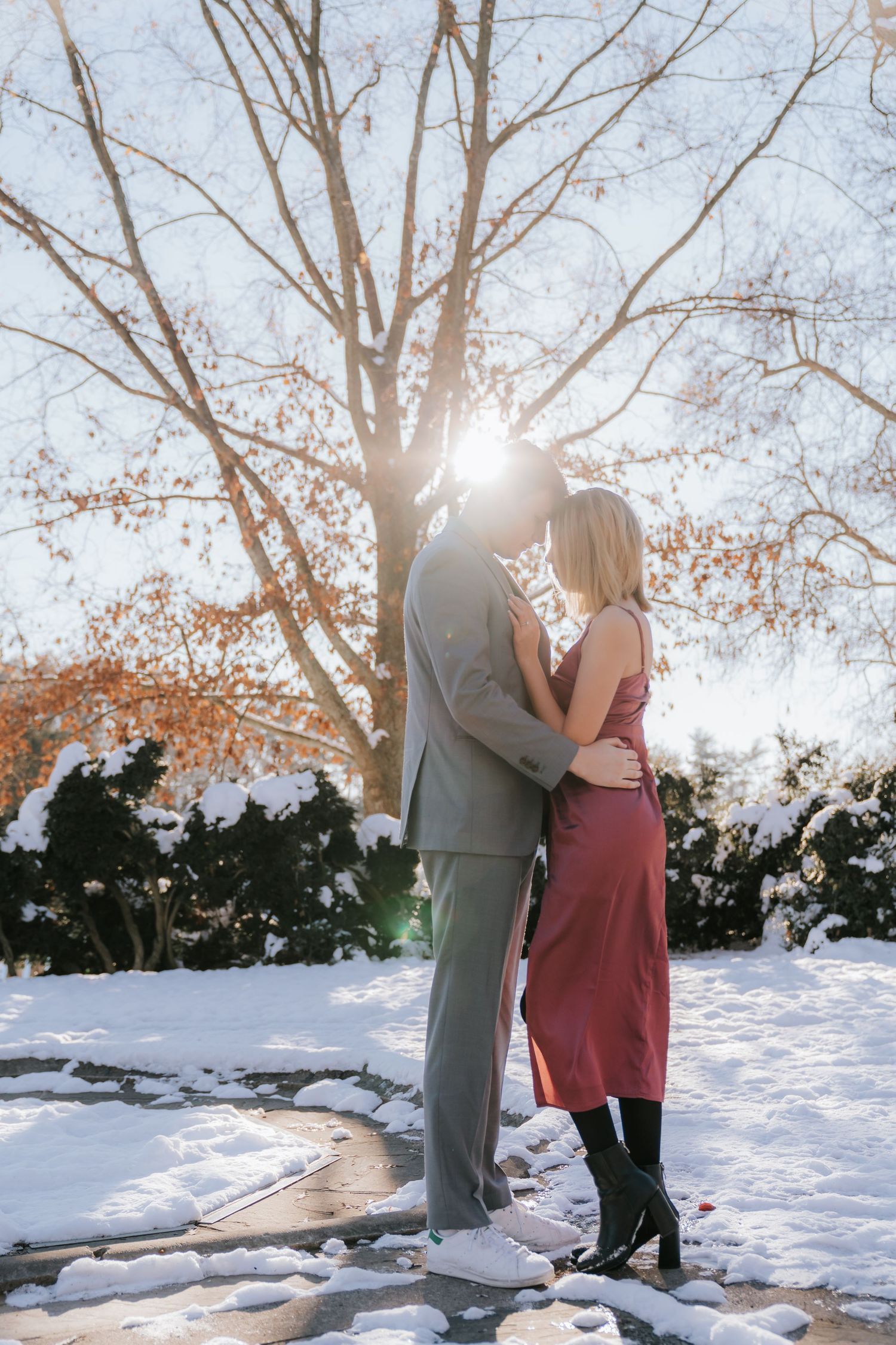 A romantic winter photoshoot with sunlight streaming through bare trees in snowy landscape.