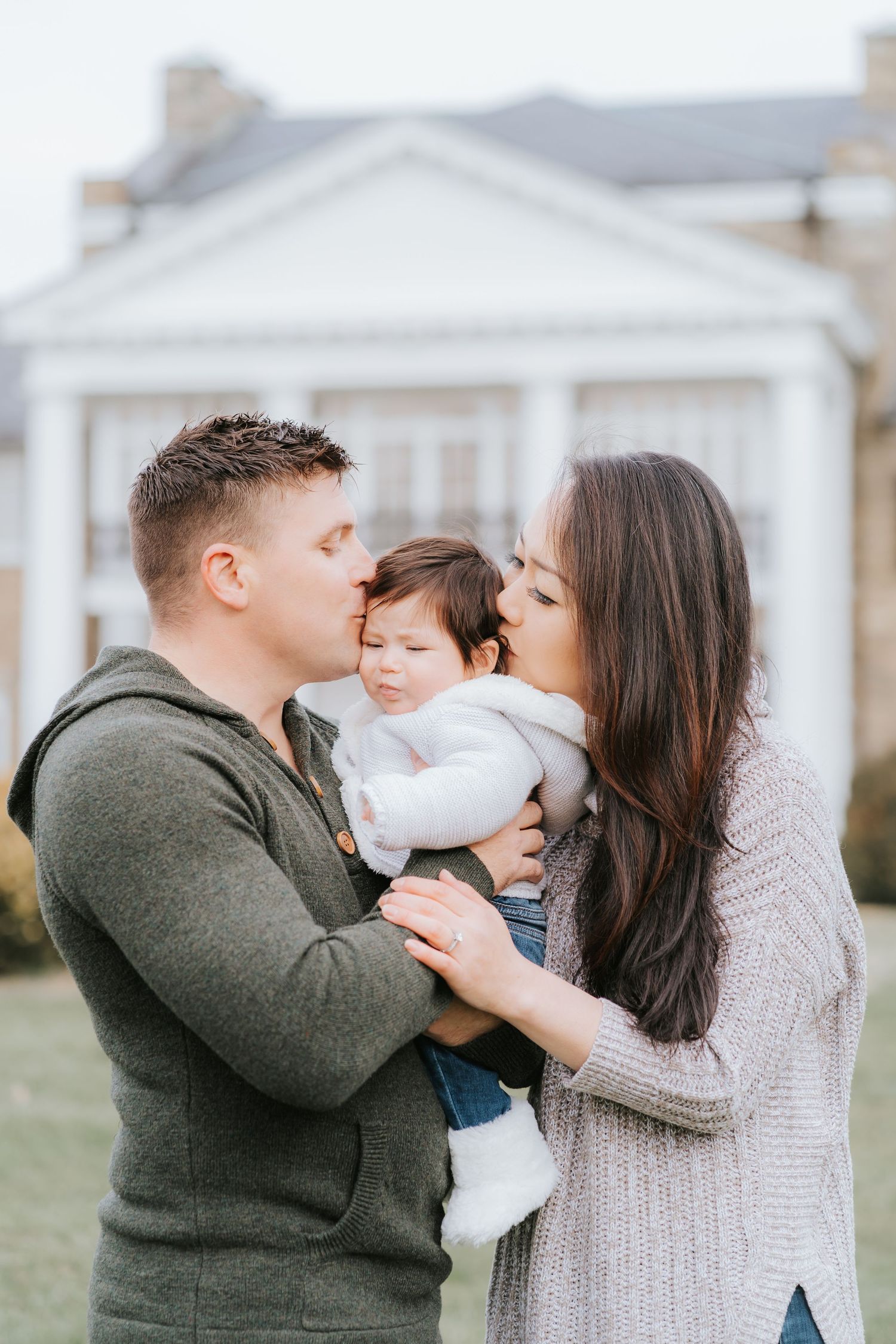 Tender family moment captured outside white colonial style home.