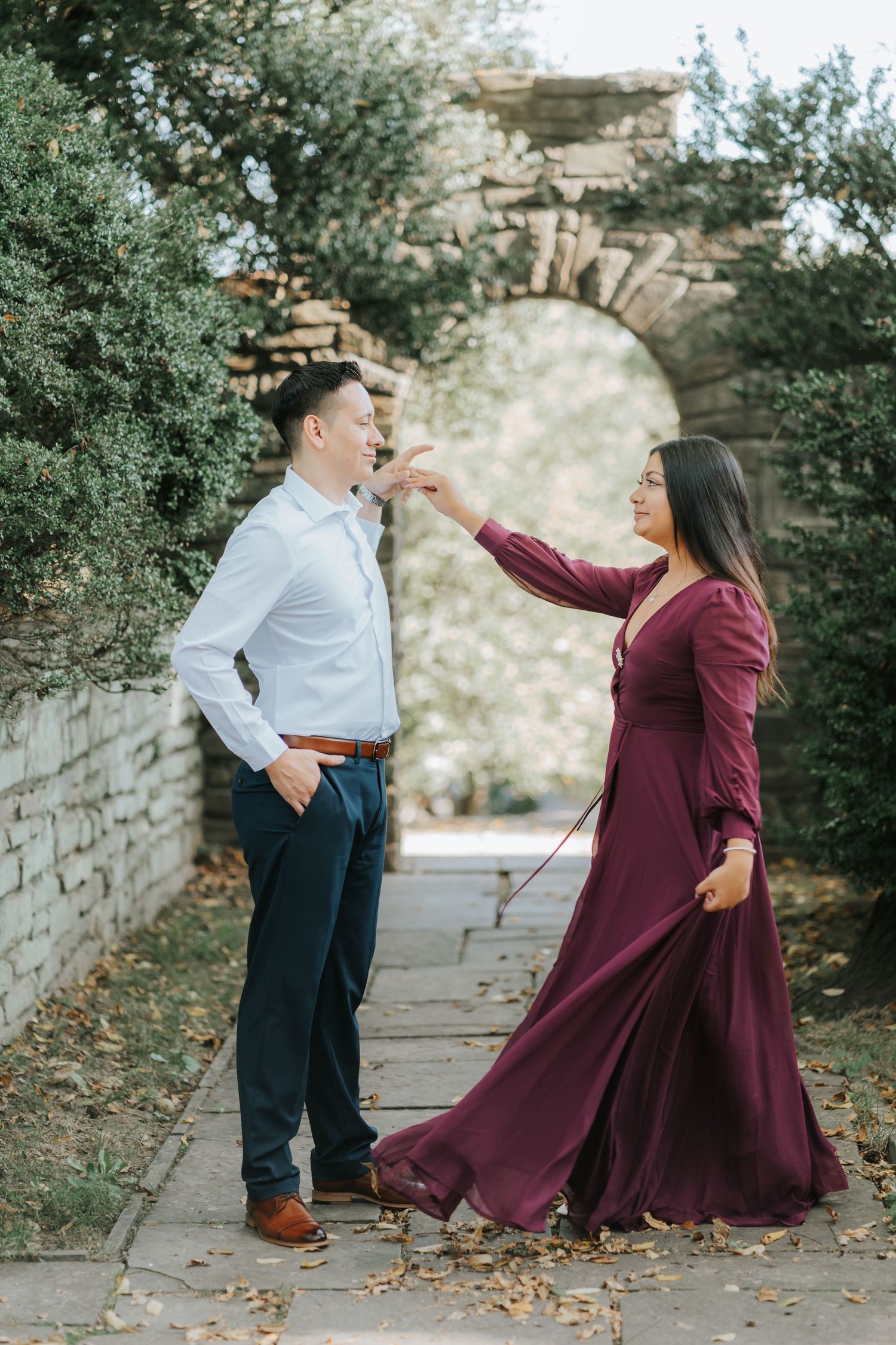 A playful engagement photo showing a couple in formal attire posing beneath a garden archway.