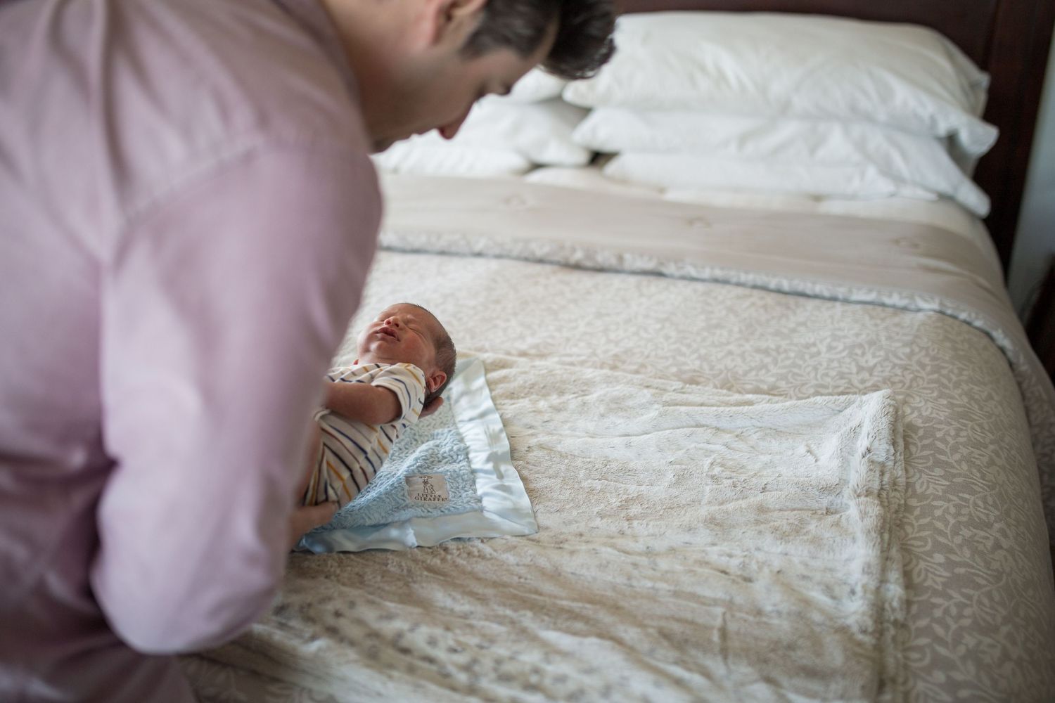 Everett newborn session: a new dad lays his newborn son down on the bed at an in-home photo session