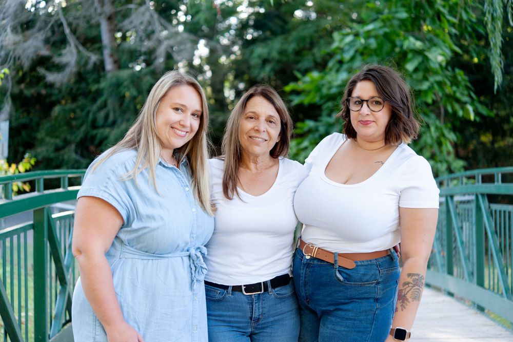 Three women in casual attire standing together on green bridge.