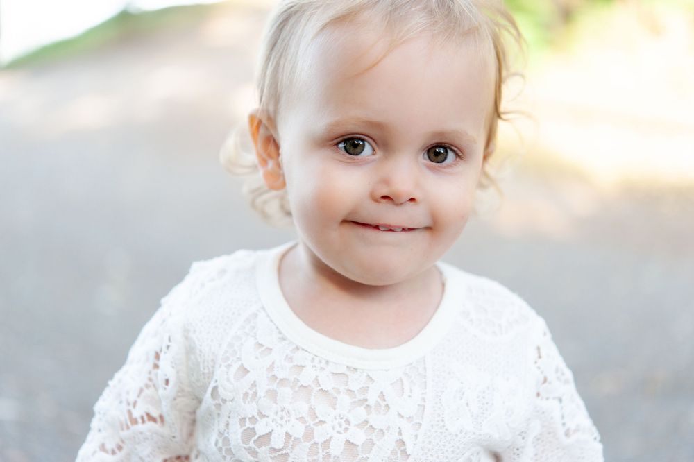 Young child in white lace dress smiling outdoors.