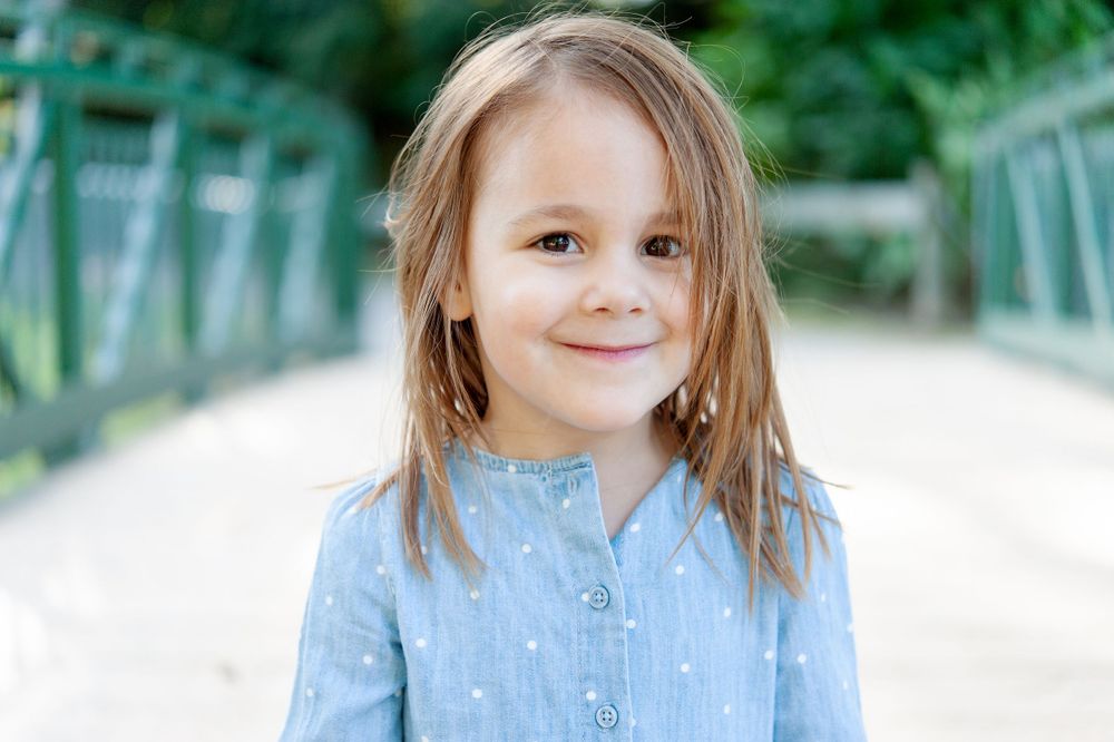 Young child in blue top smiling on bridge outdoors.