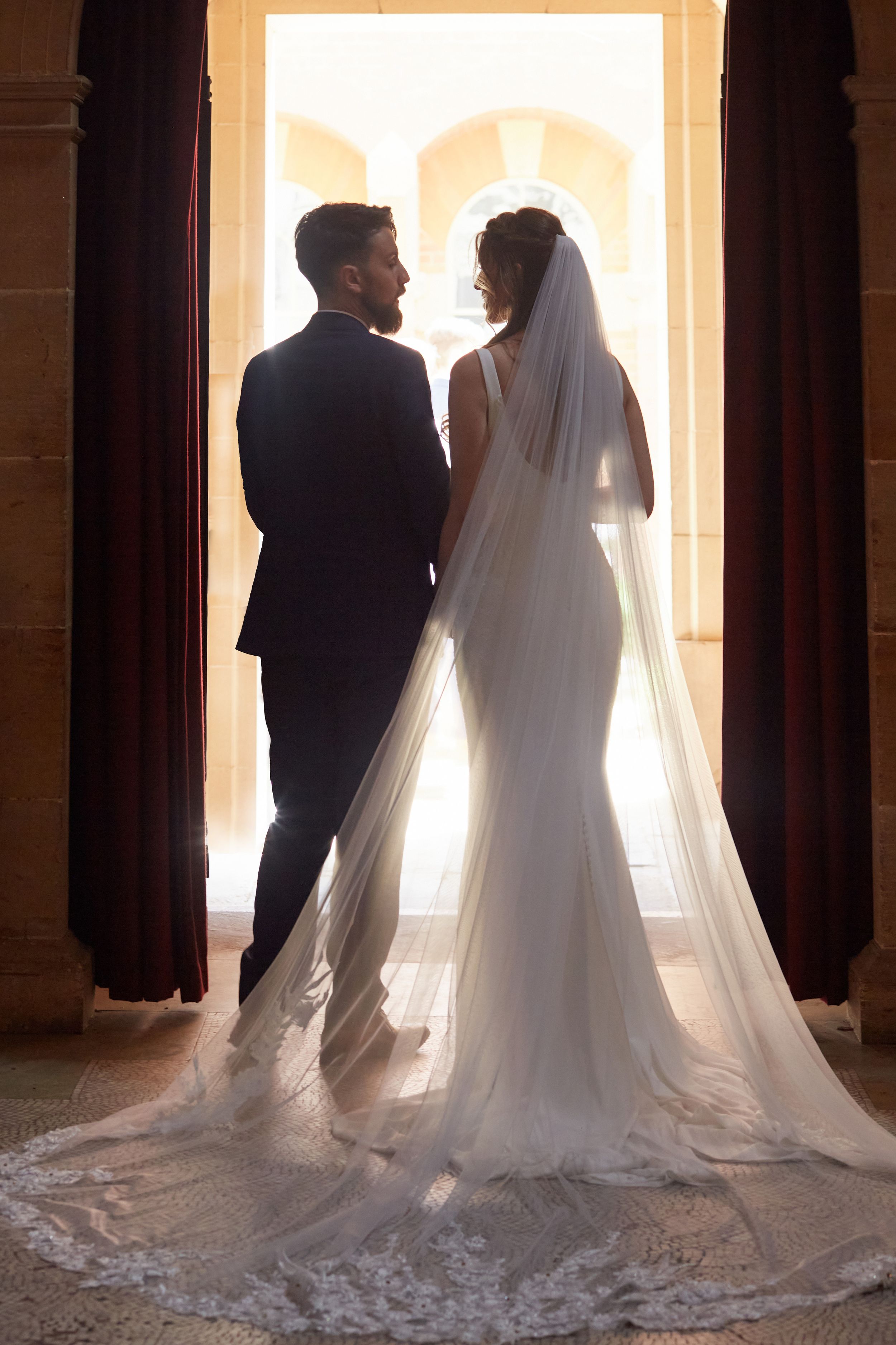 Silhouette of a bride and groom standing in an arched doorway with dramatic backlighting.