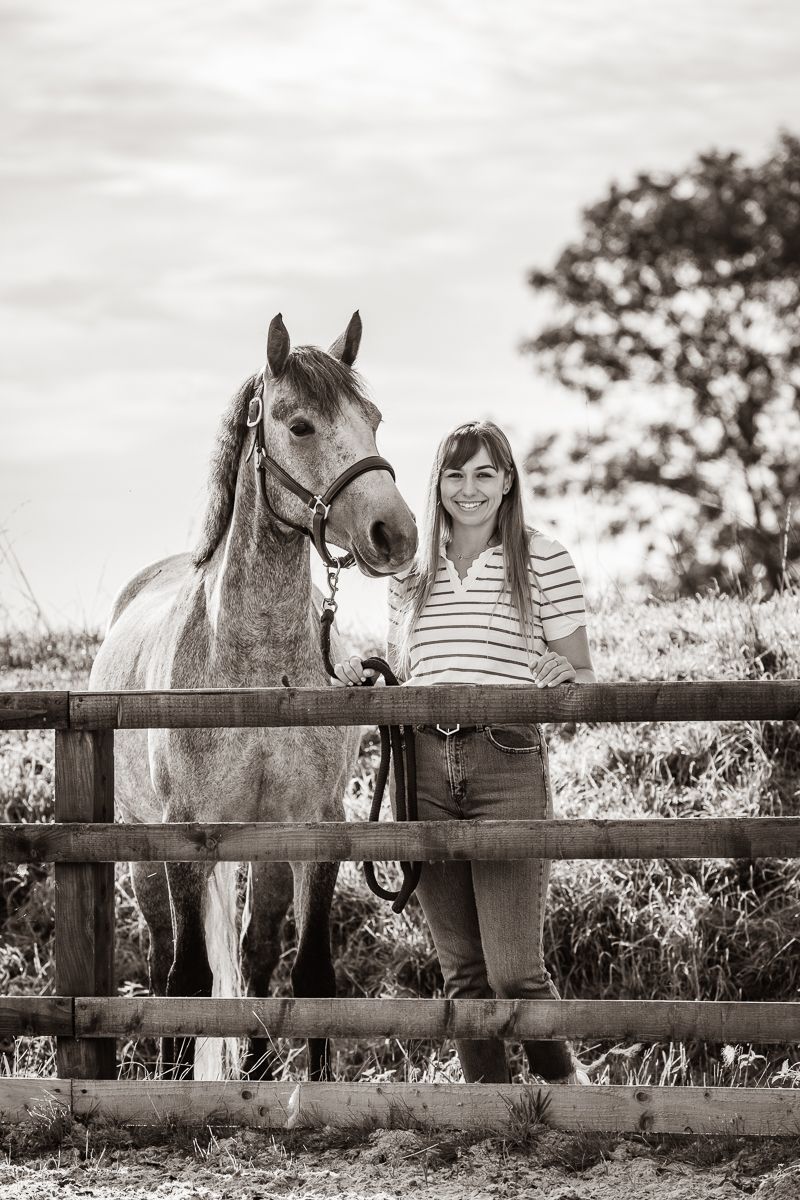 A grey horse and companion stand at a wooden fence for a black and white portrait.