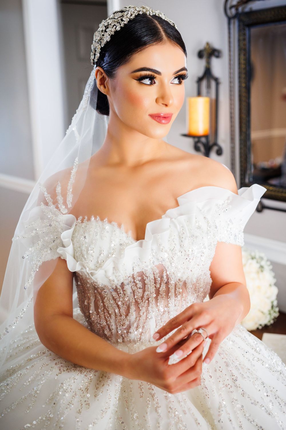 A regal bride in a sparkly white ball gown and crystal headpiece poses elegantly before her wedding ceremony.