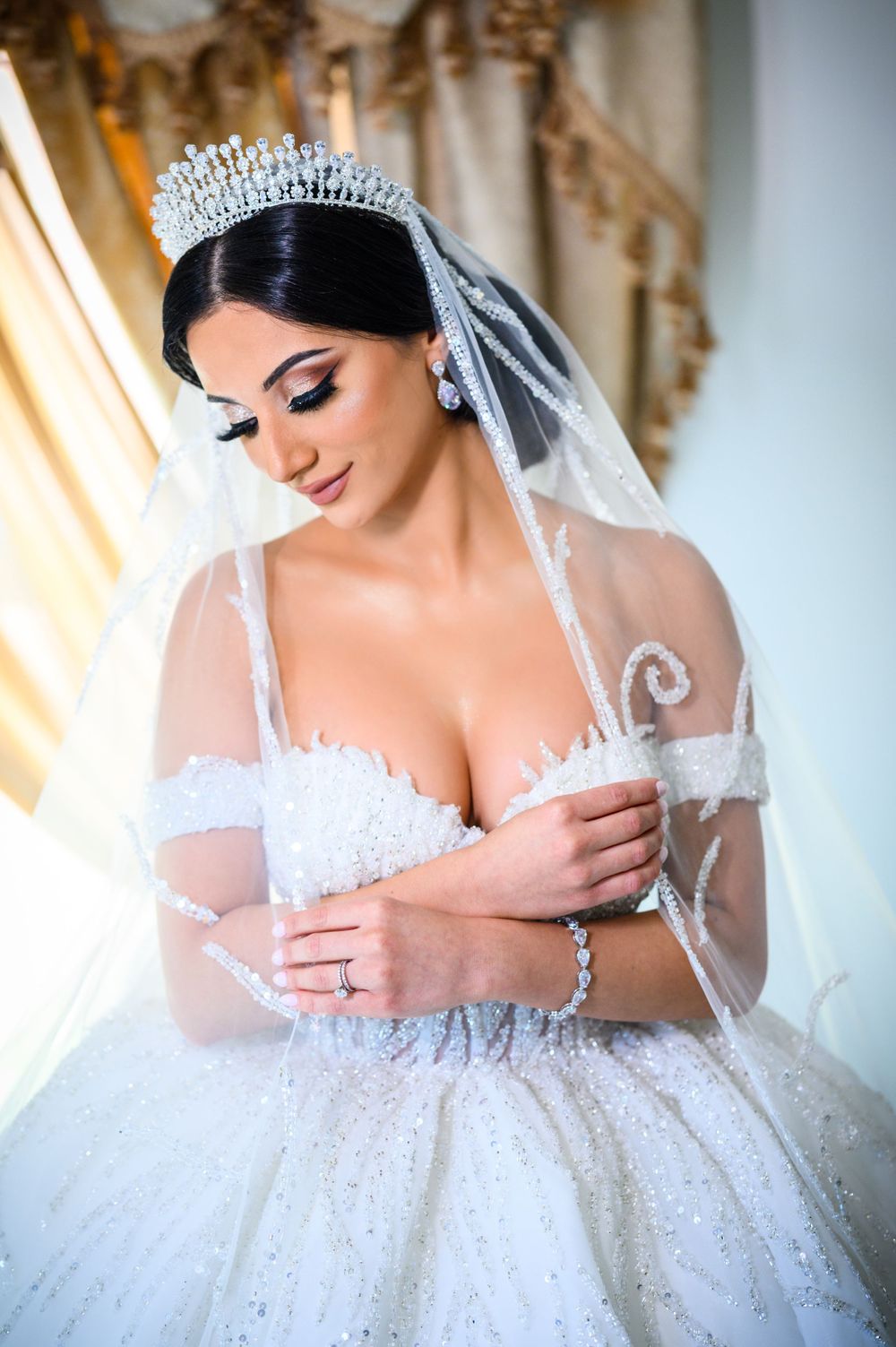 Elegant bridal portrait showcasing intricate lace dress and crystal crown with dramatic lighting.