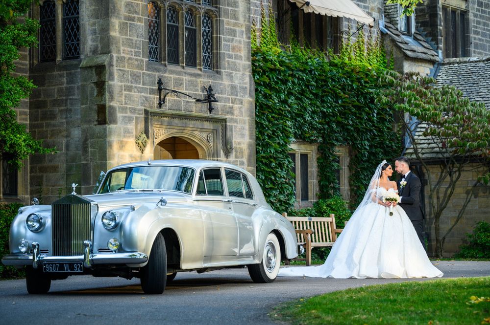 Classic white Rolls Royce parked outside gothic stone church with ivy covered walls.
