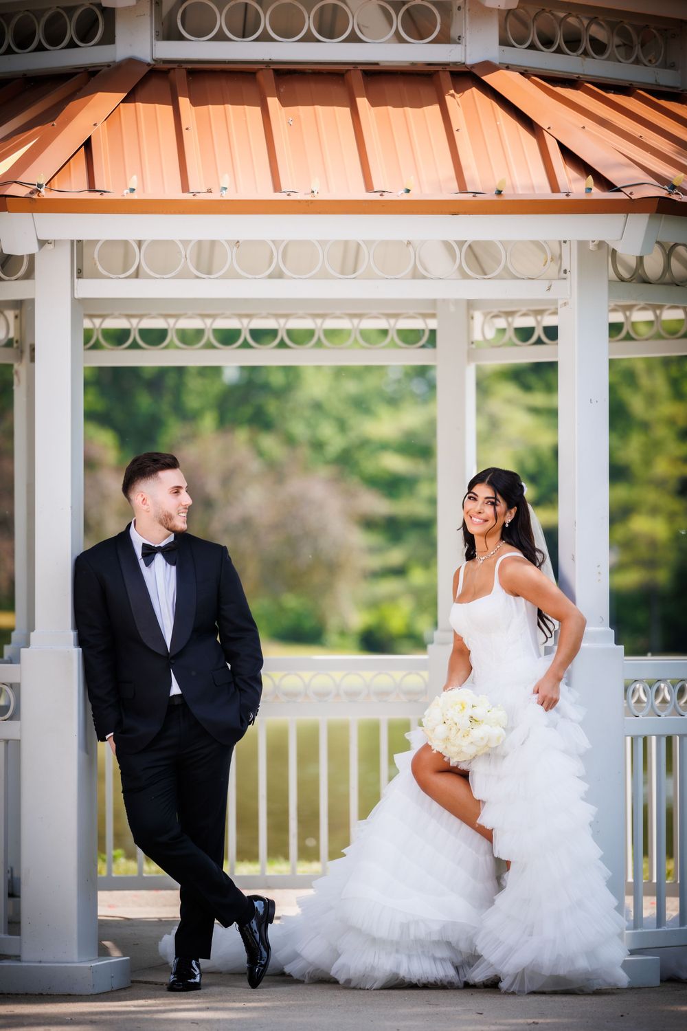 A wedding couple poses together under a white gazebo with copper roof details.