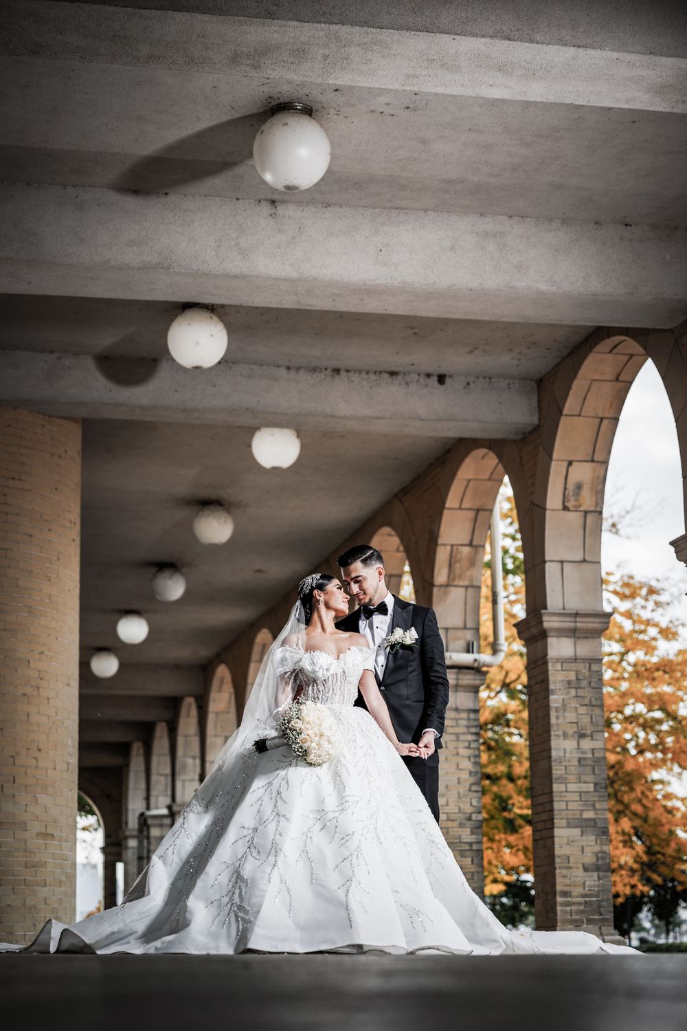 Wedding couple poses under arched colonnade with spherical lights creating dramatic perspective.