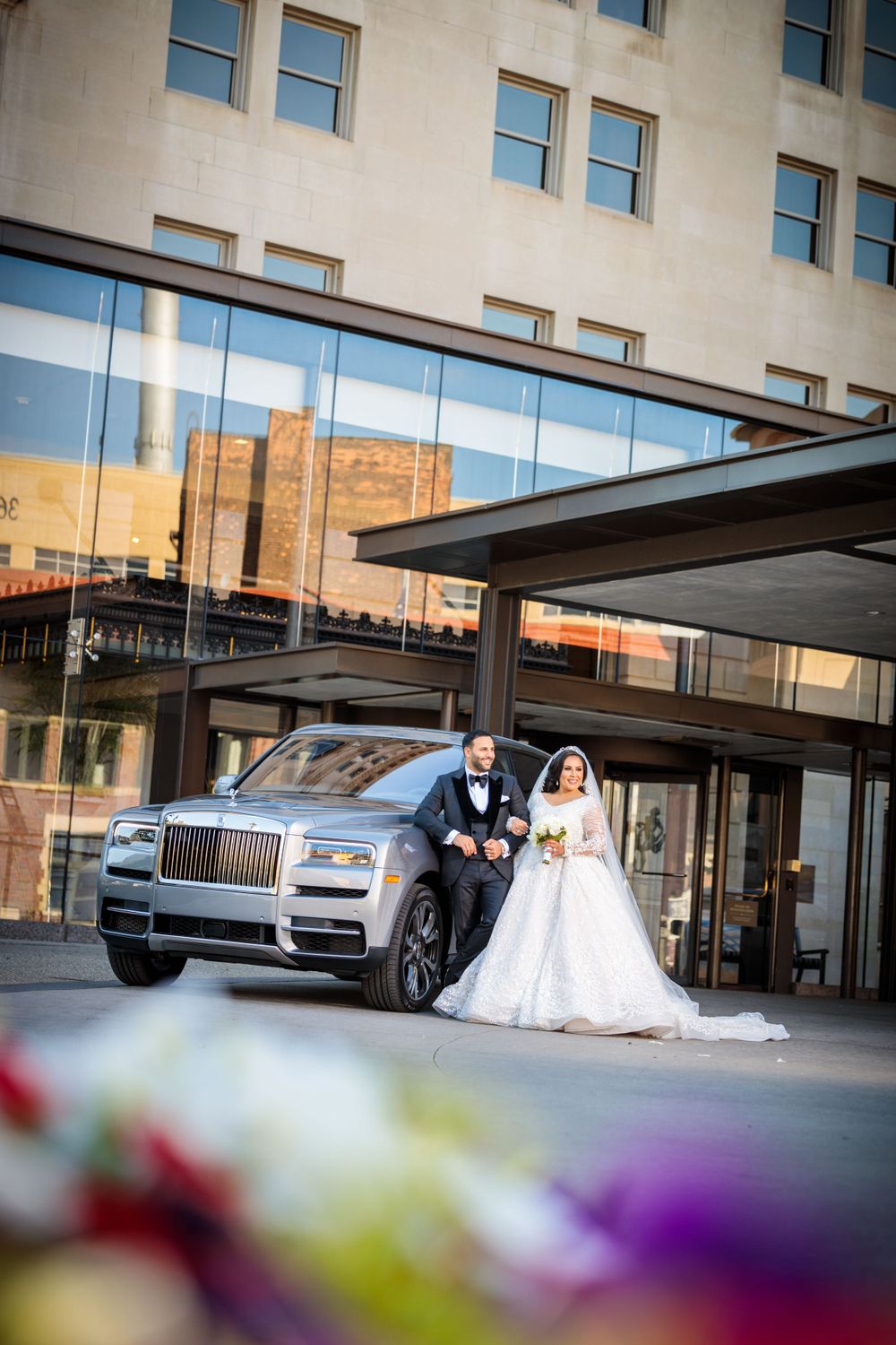 Luxurious wedding photo featuring a Rolls Royce and elegant decor outside a modern building.