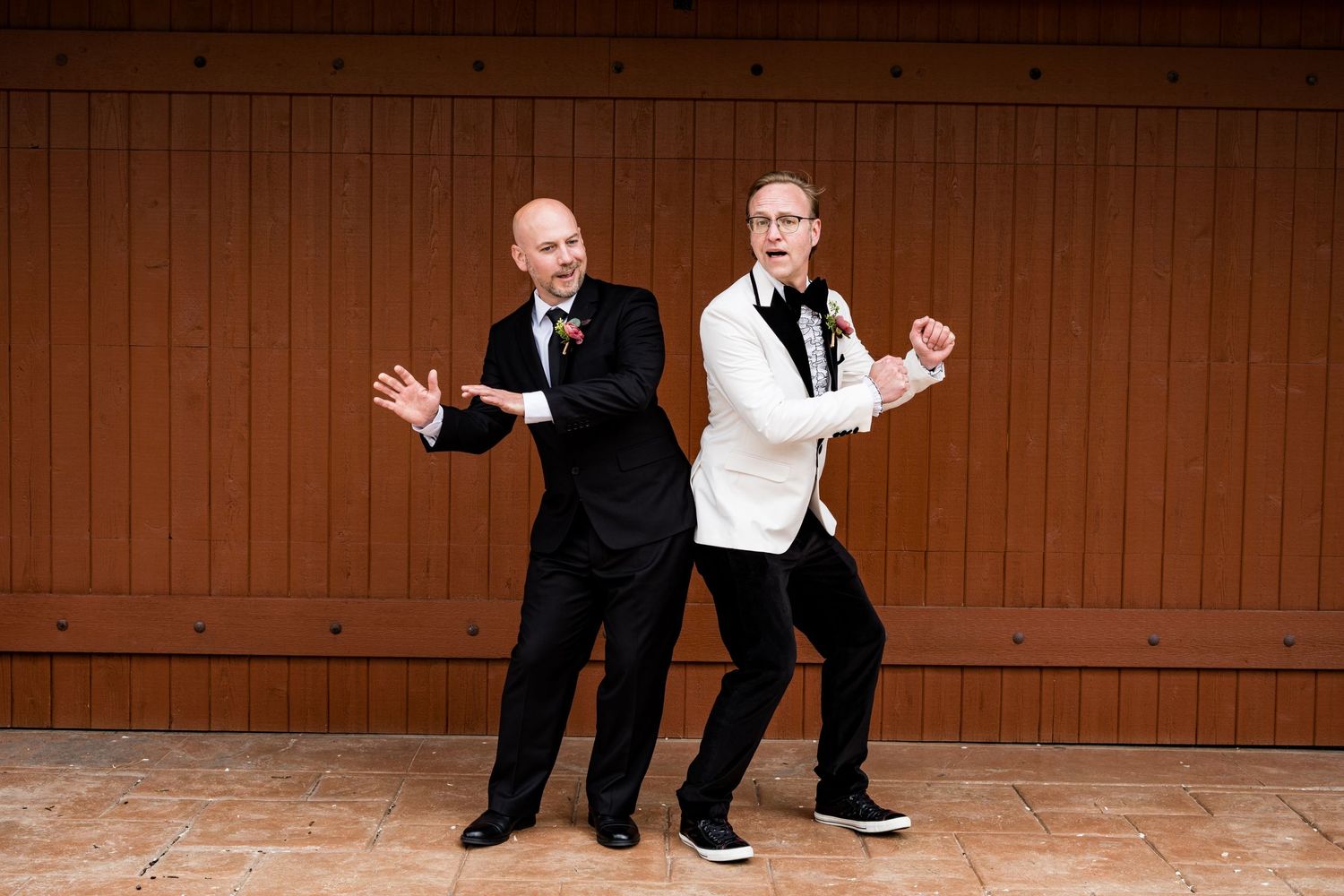 Two people strike fun dance poses against a wooden wall backdrop.