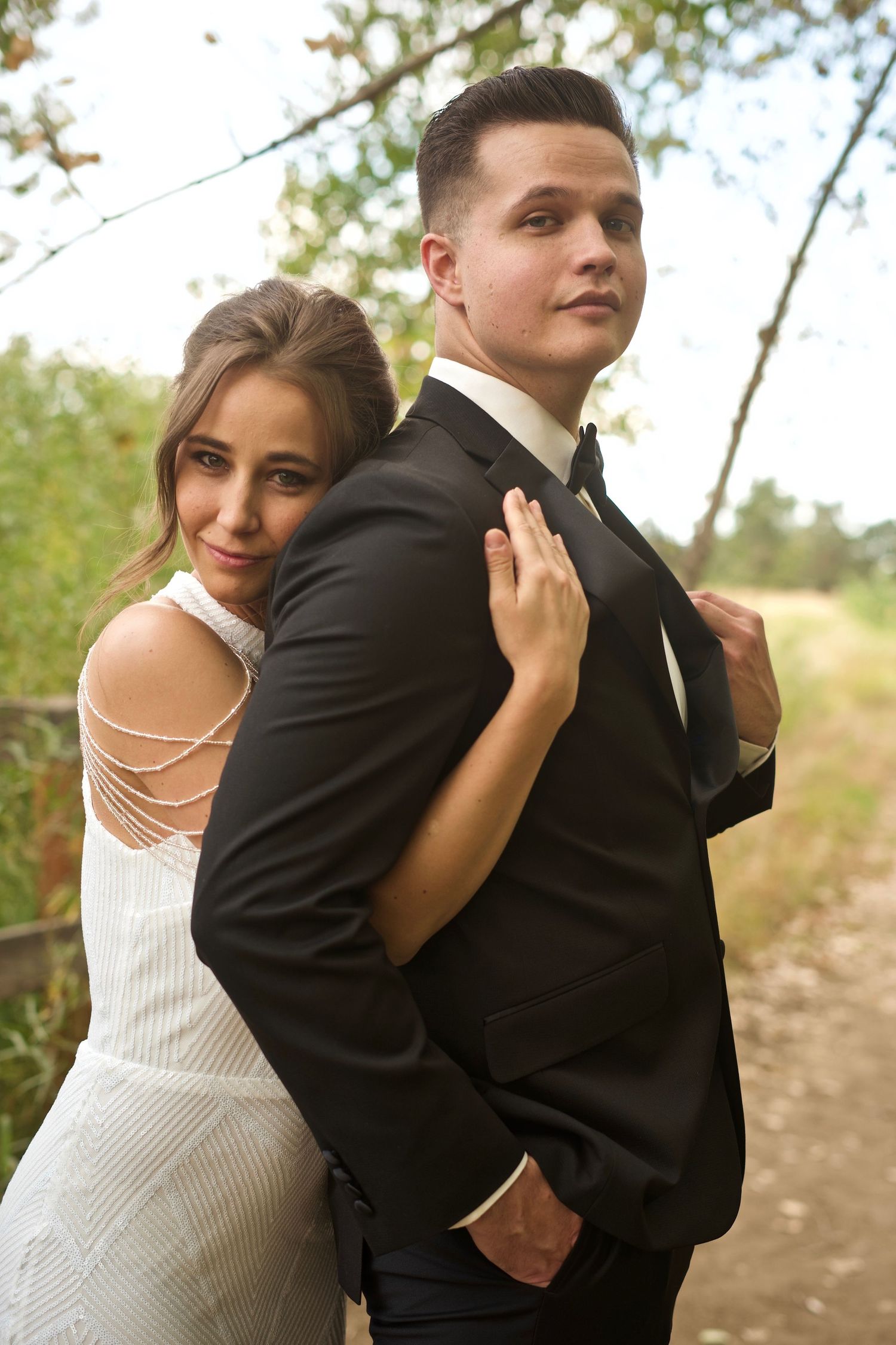 A romantic wedding portrait of a couple in an intimate embrace in formal attire on a nature path.