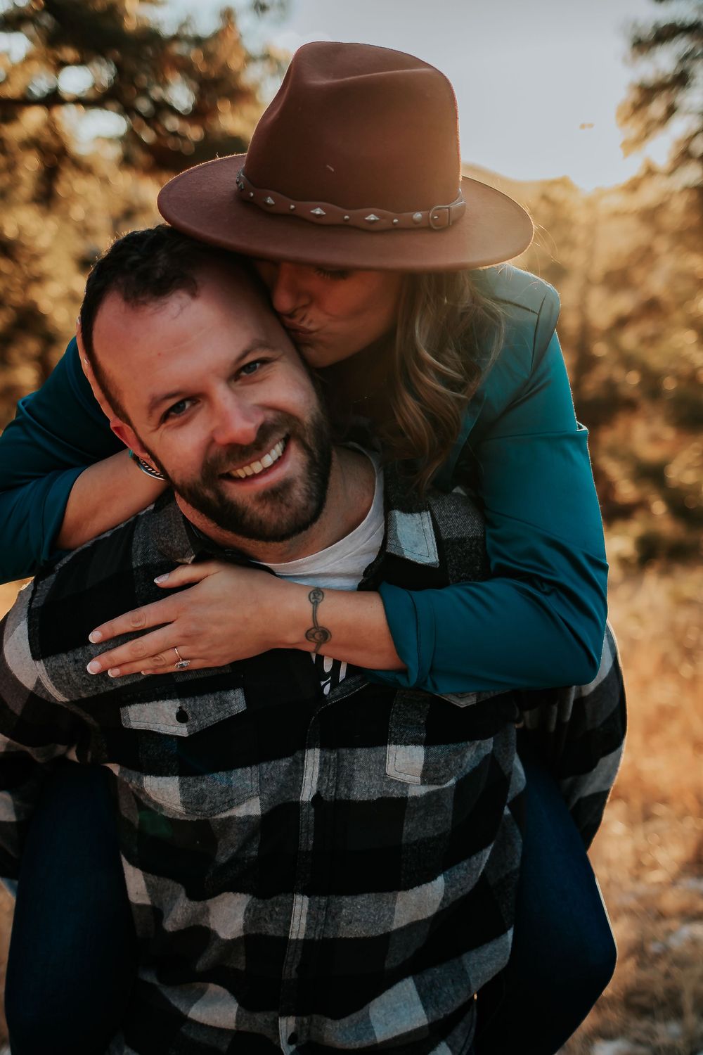Playful piggyback ride moment in golden sunlight with couple in casual outdoor attire. Colorado engagement photography.