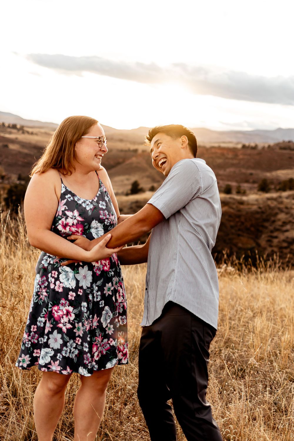 Couple laughing together in a scenic mountain field during golden hour. Fort Collins Engagement Photography.