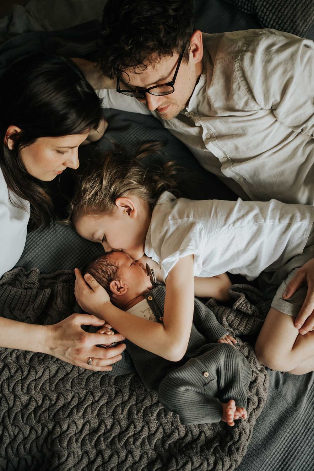 noworodek, brat, mama i tata leżą na łóżku - fotograf Kraków
