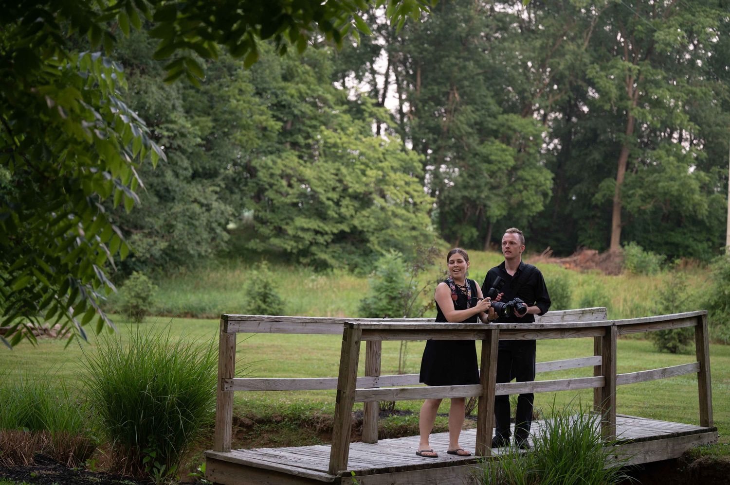 Couple standing together on wooden bridge in garden setting.