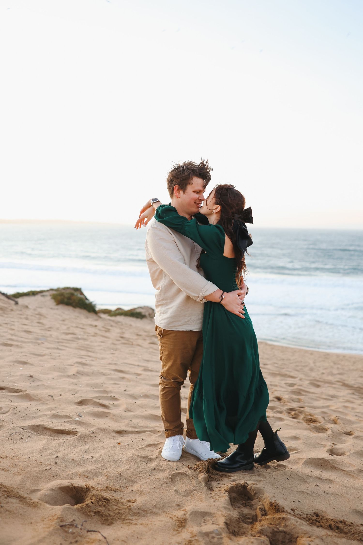 A tender embrace between two people on a sandy beach with waves crashing in the background.
