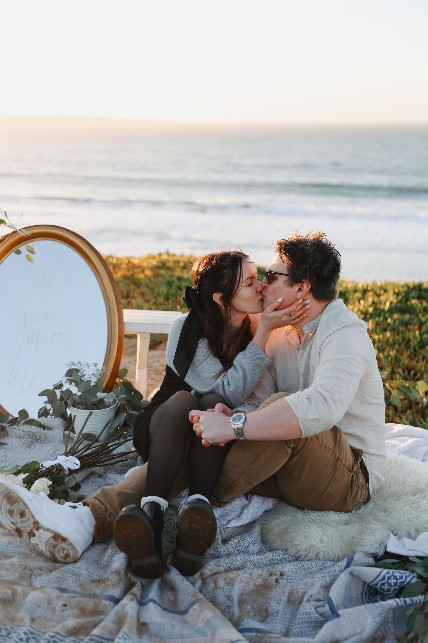 Intimate moment shared during sunset beach picnic with decorative mirror and blanket setup.