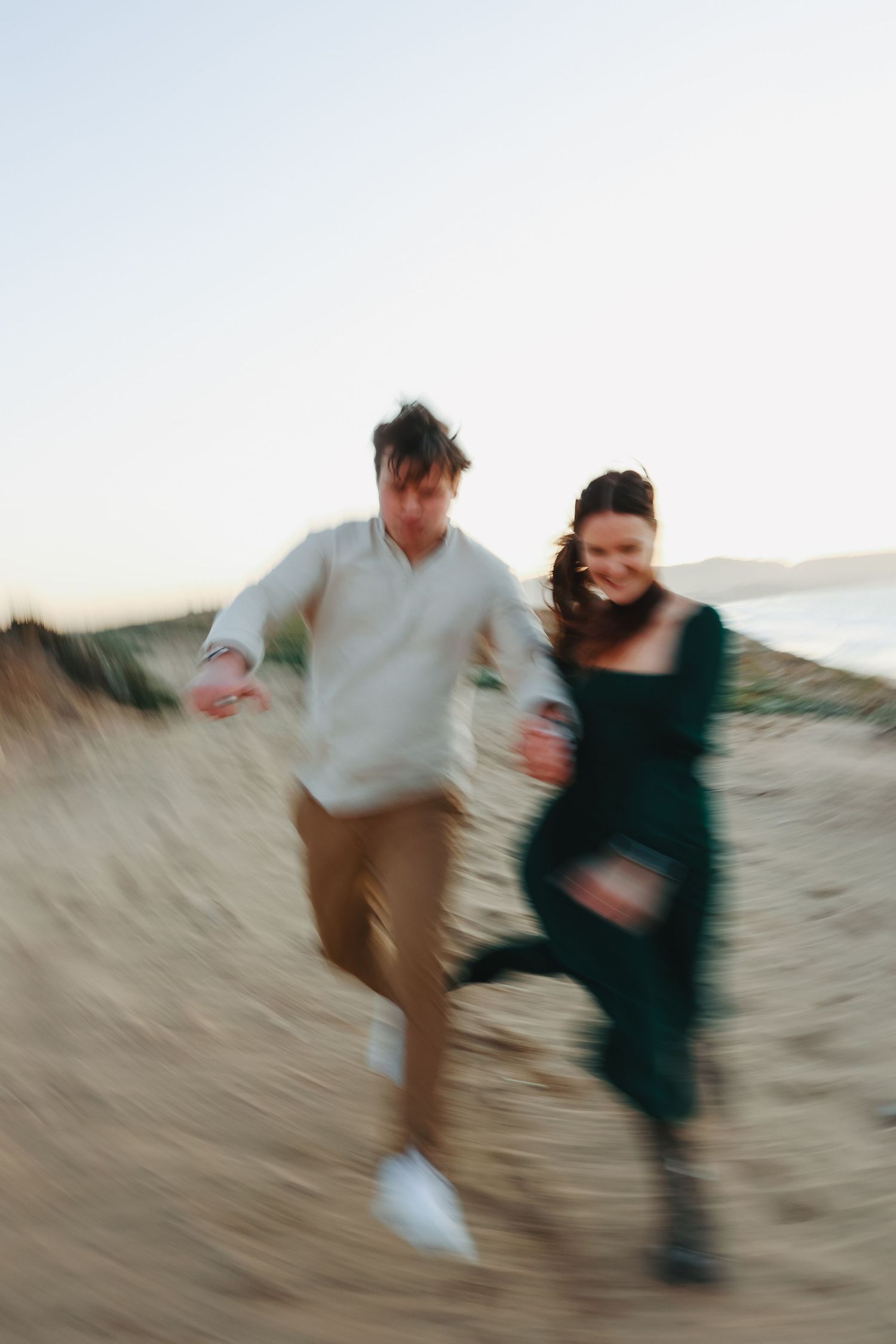 A blurred motion shot captures a couple running playfully on a beach at sunset.