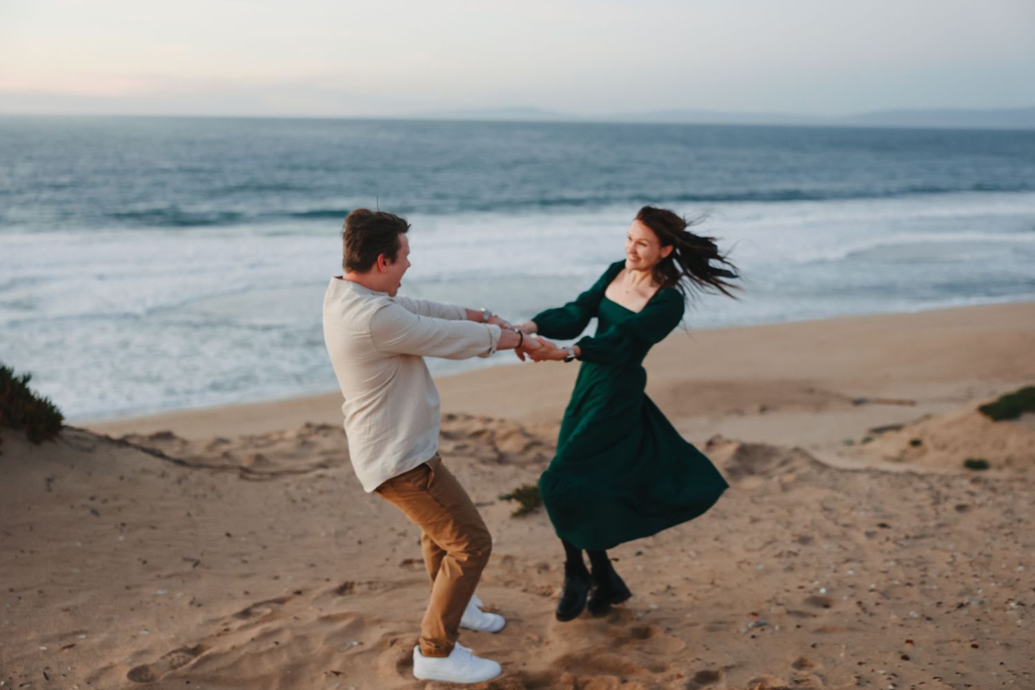 A couple spins in a romantic dance on a beach with crashing waves in the background.