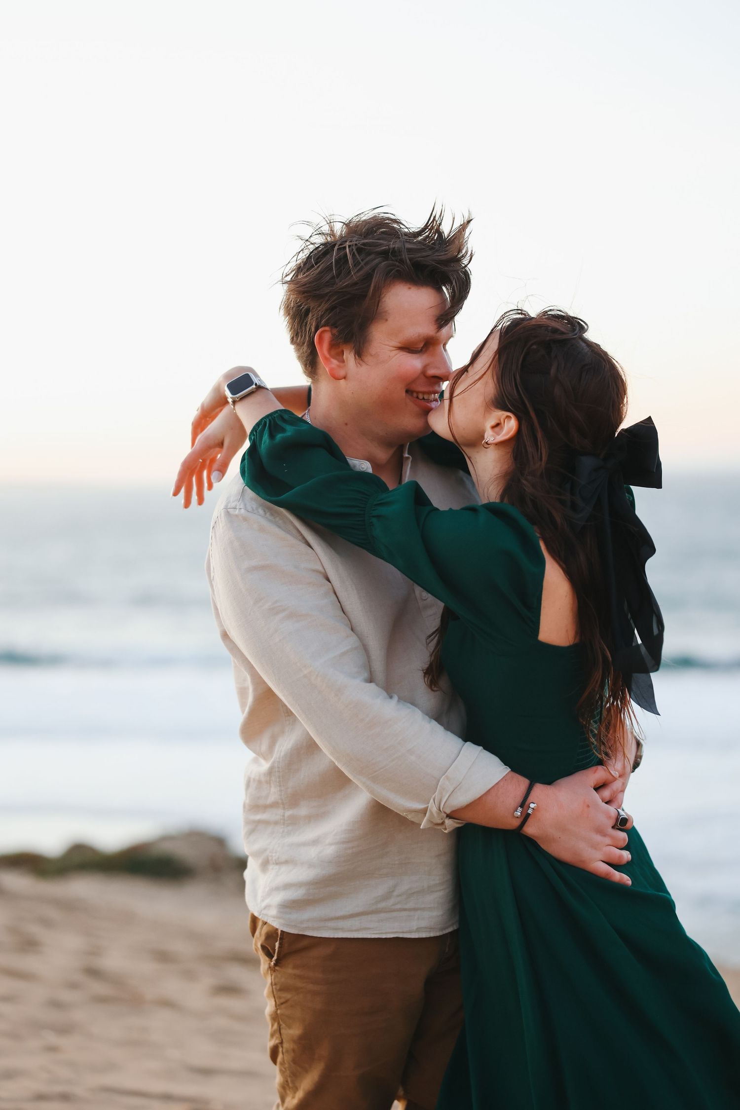 A romantic moment captured between two people in casual wear on a beach during golden hour.
