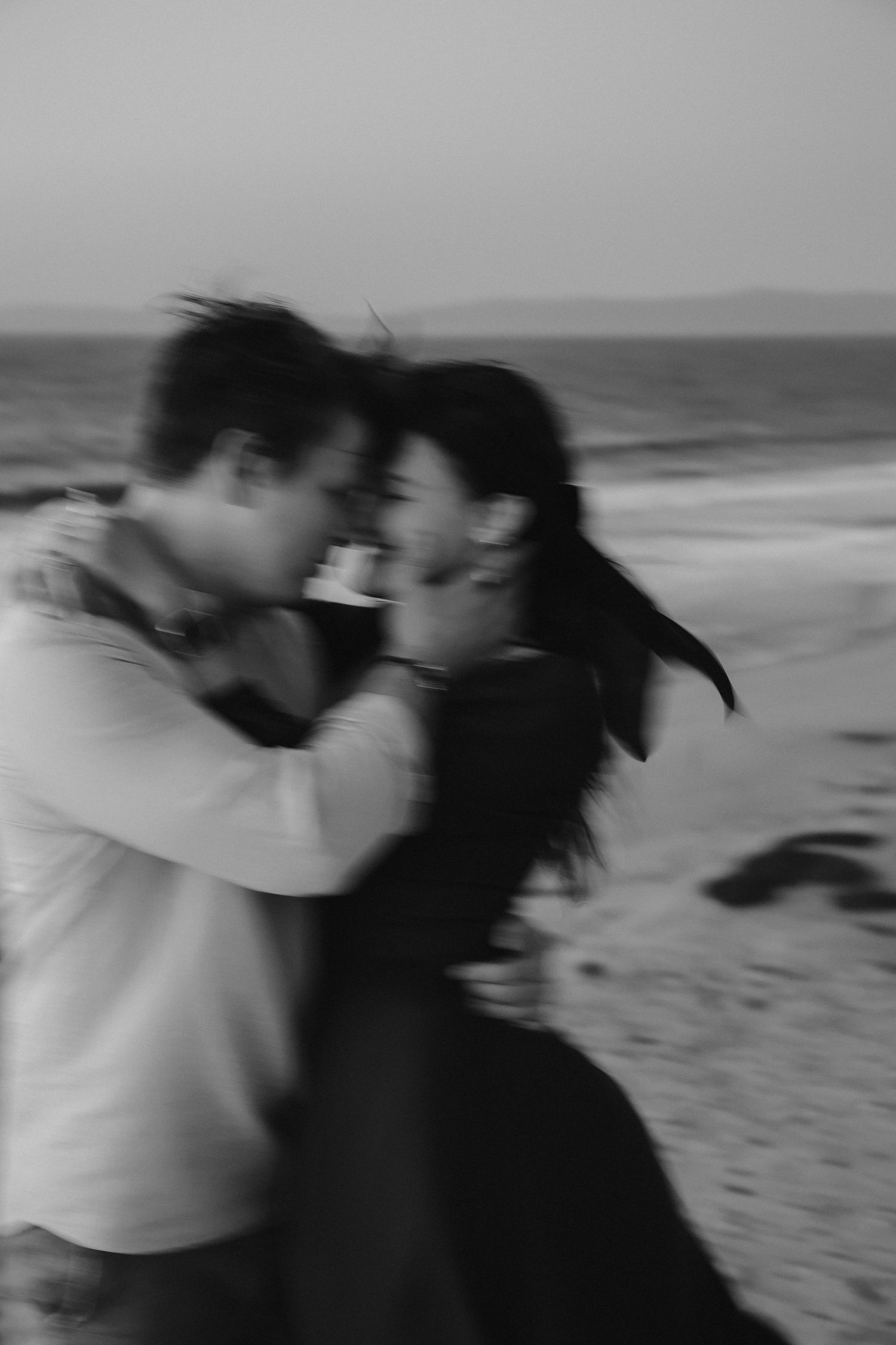 A blurred artistic photo captures an intimate moment between two people on a beach at dusk.