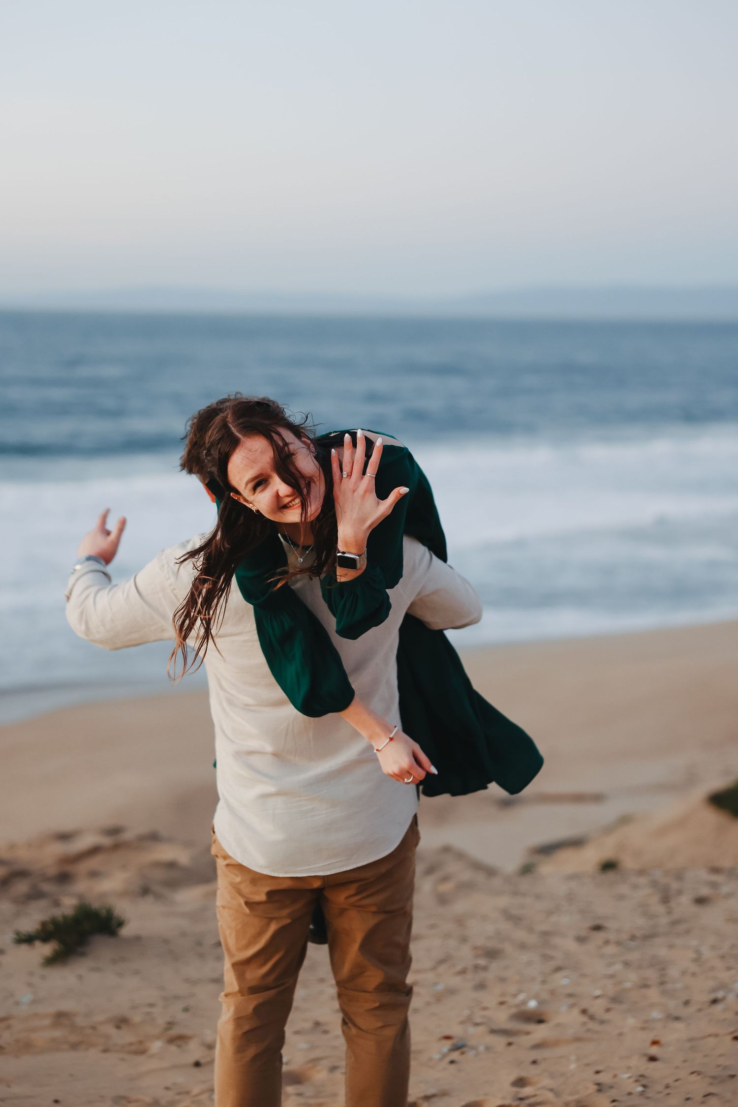 Candid beach photo captures joyful laughter during a piggyback ride along the shore.