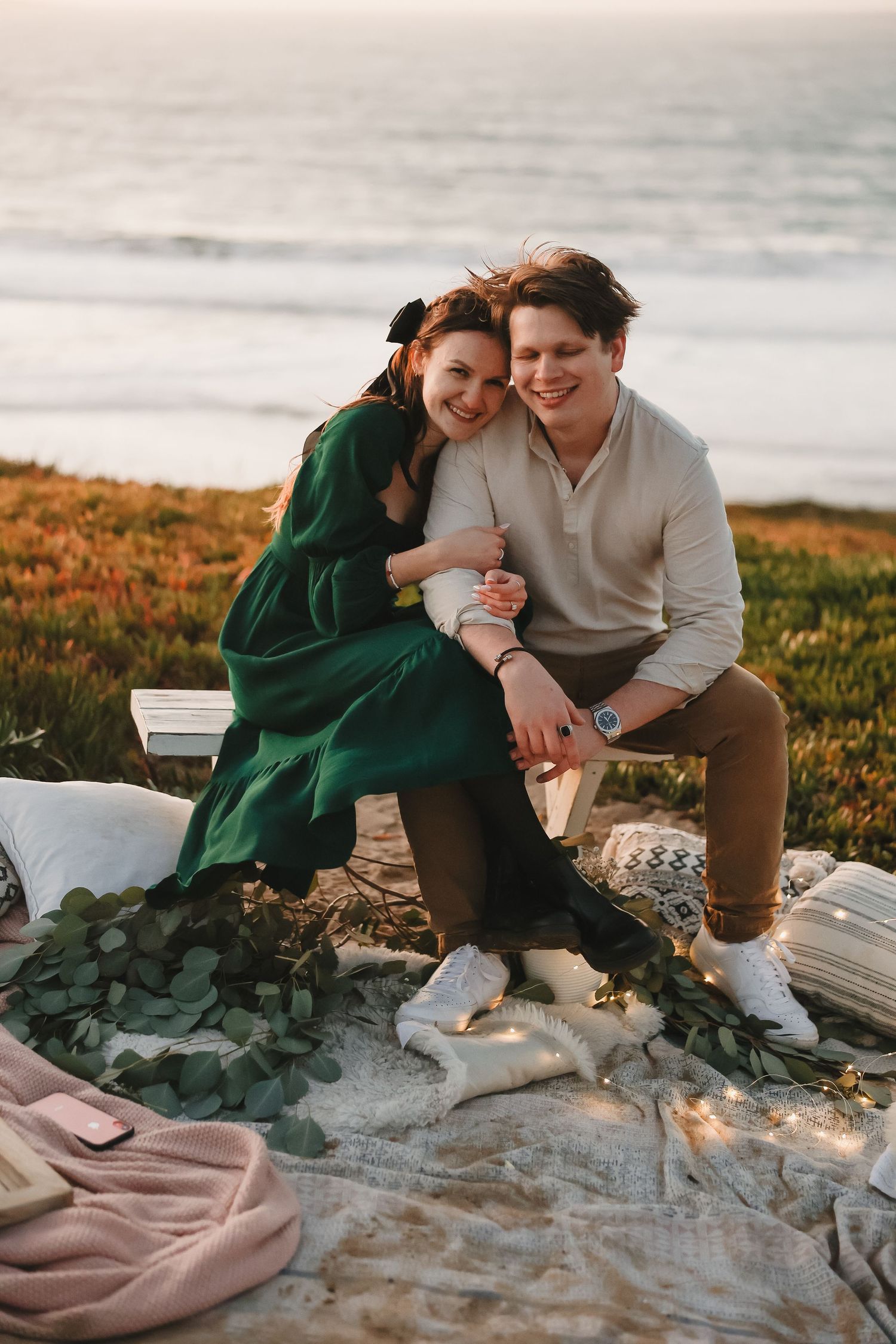 Intimate coastal picnic scene with warm lighting and blankets overlooking the ocean waves.