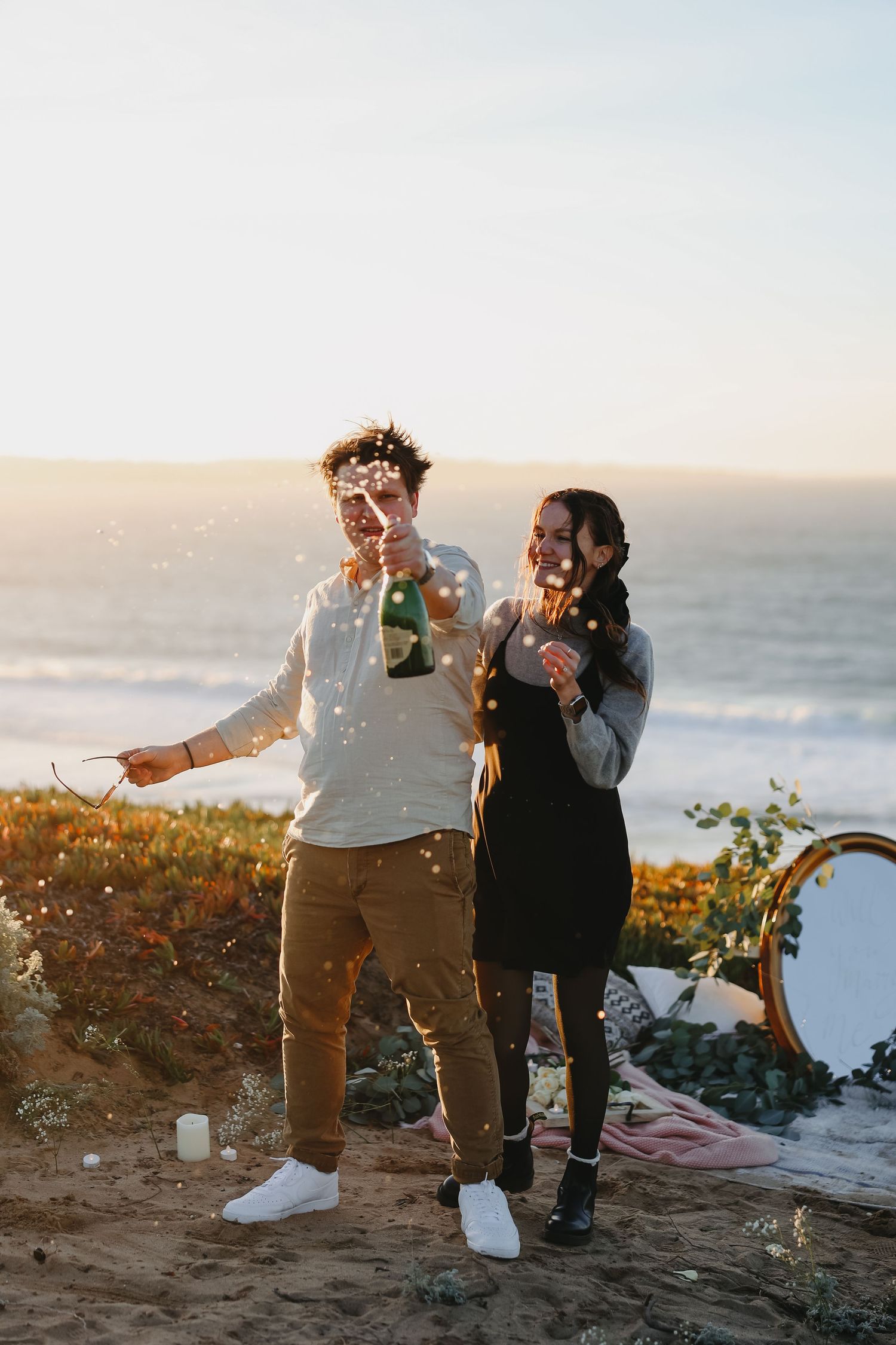 A happy couple enjoying champagne and confetti during their seaside engagement celebration.