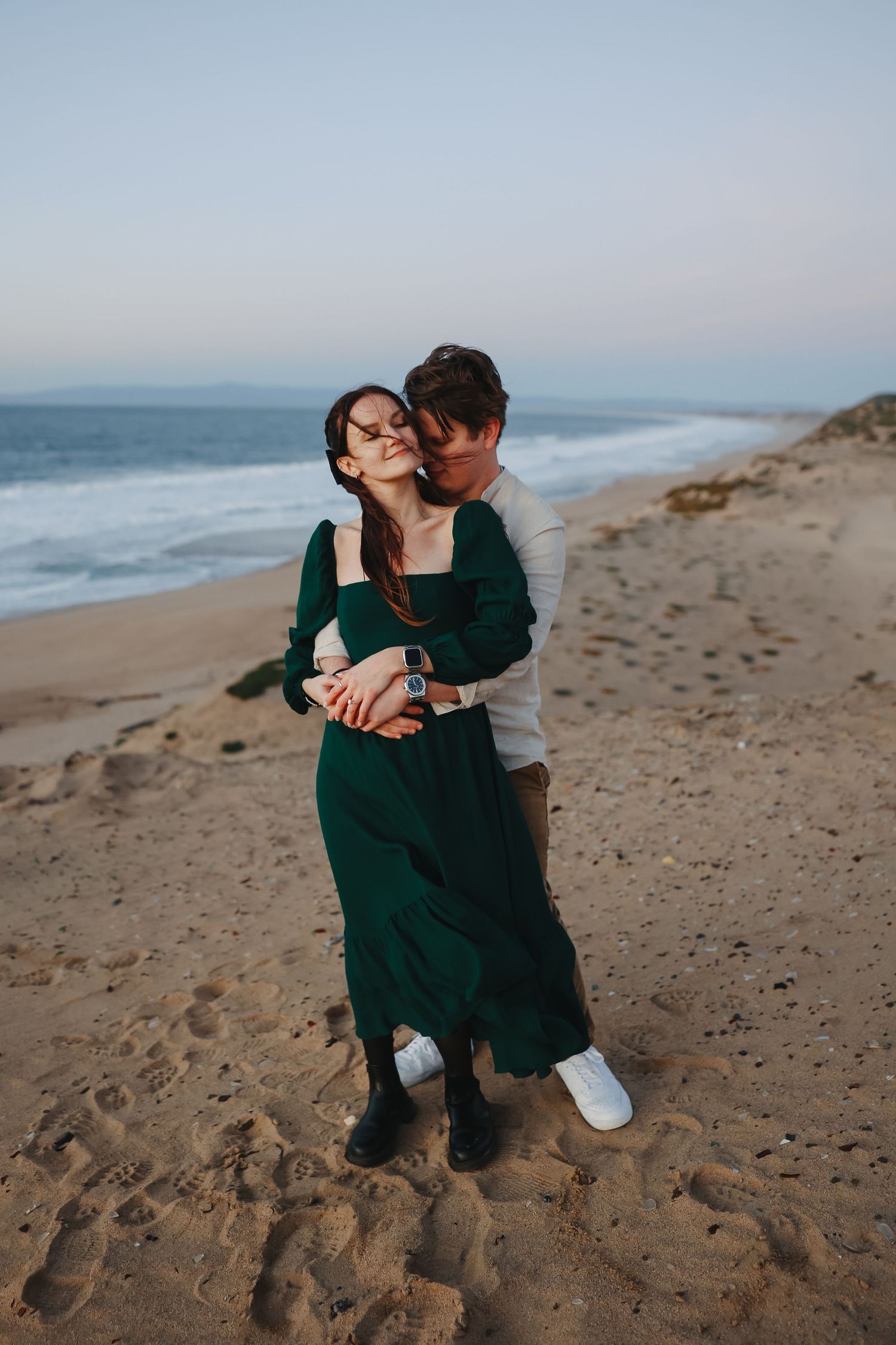 A joyful couple shares a tender moment on a sandy beach with crashing waves in the background.
