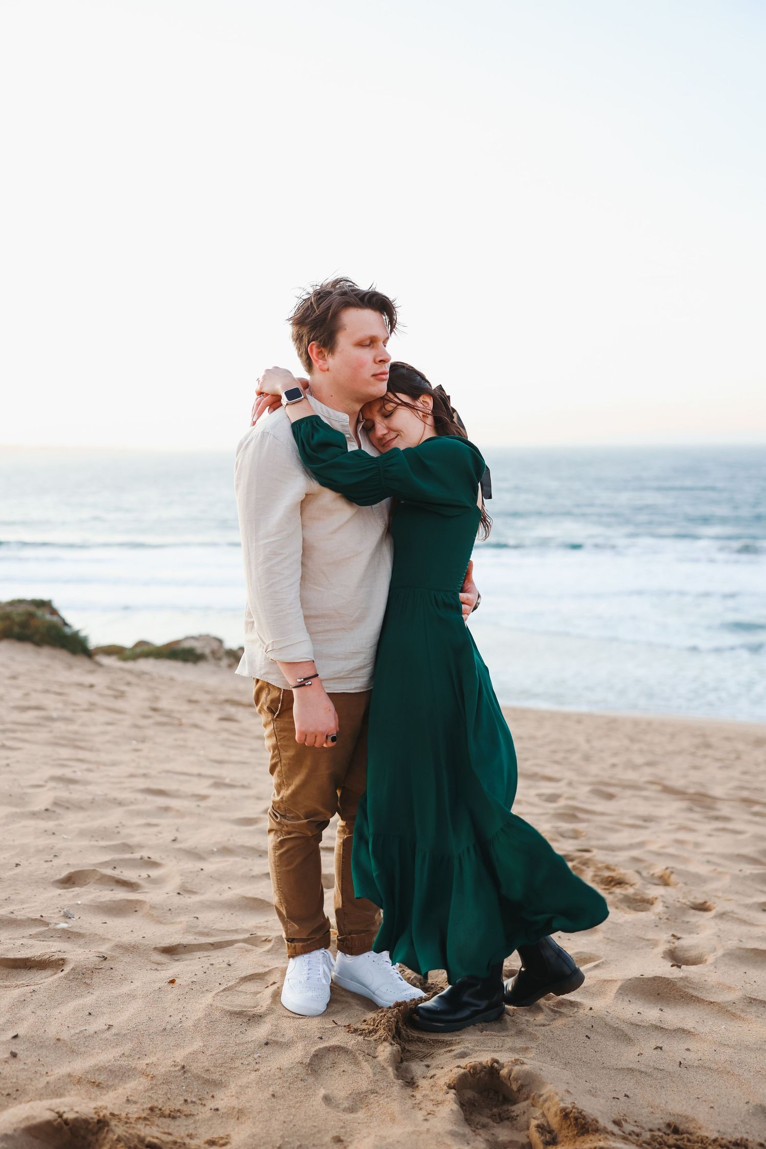 A couple in contrasting outfits shares an embrace on a sandy beach near the ocean.