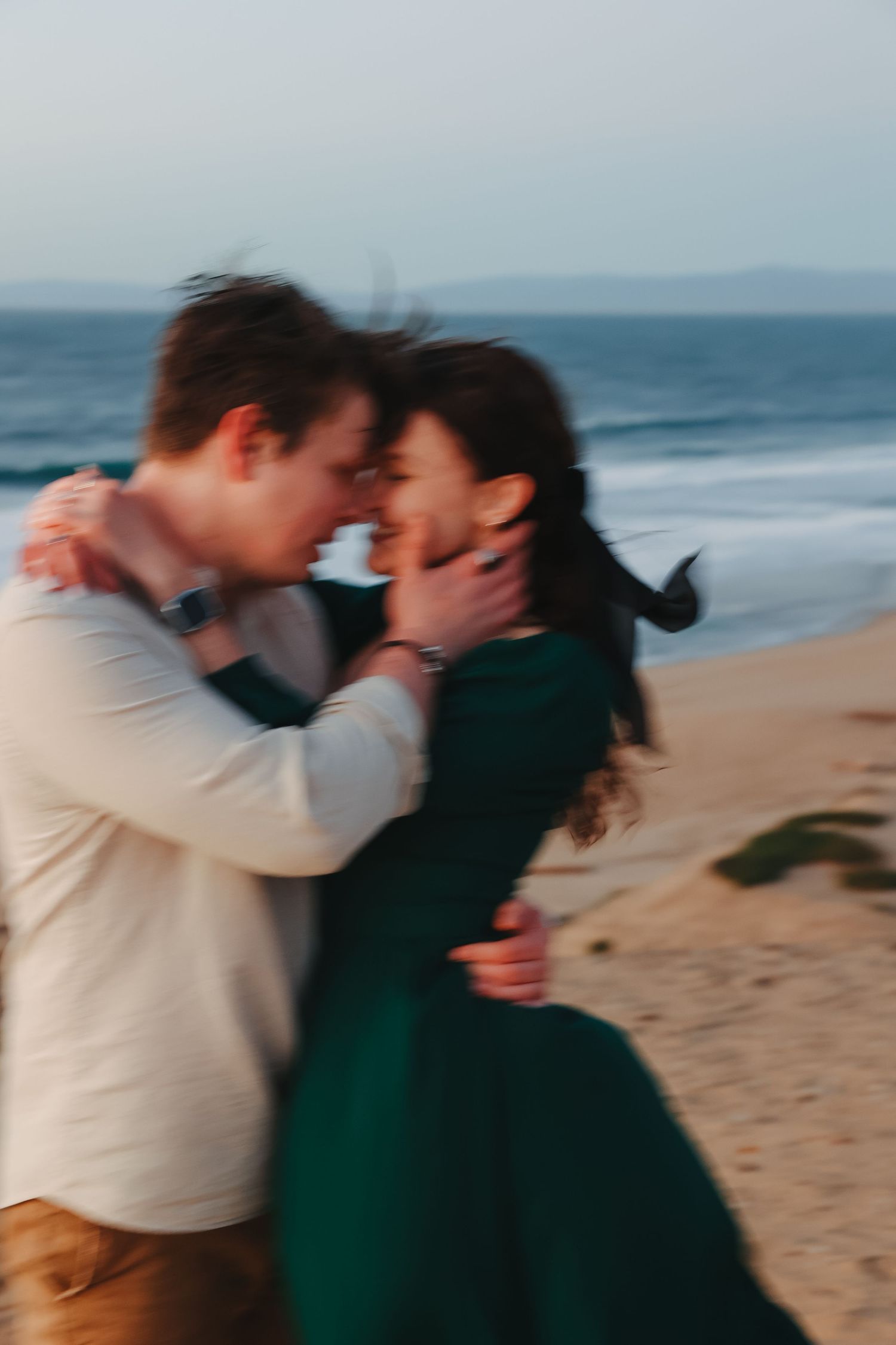 A candid moment of affection between two people in contrasting outfits against an oceanfront backdrop.