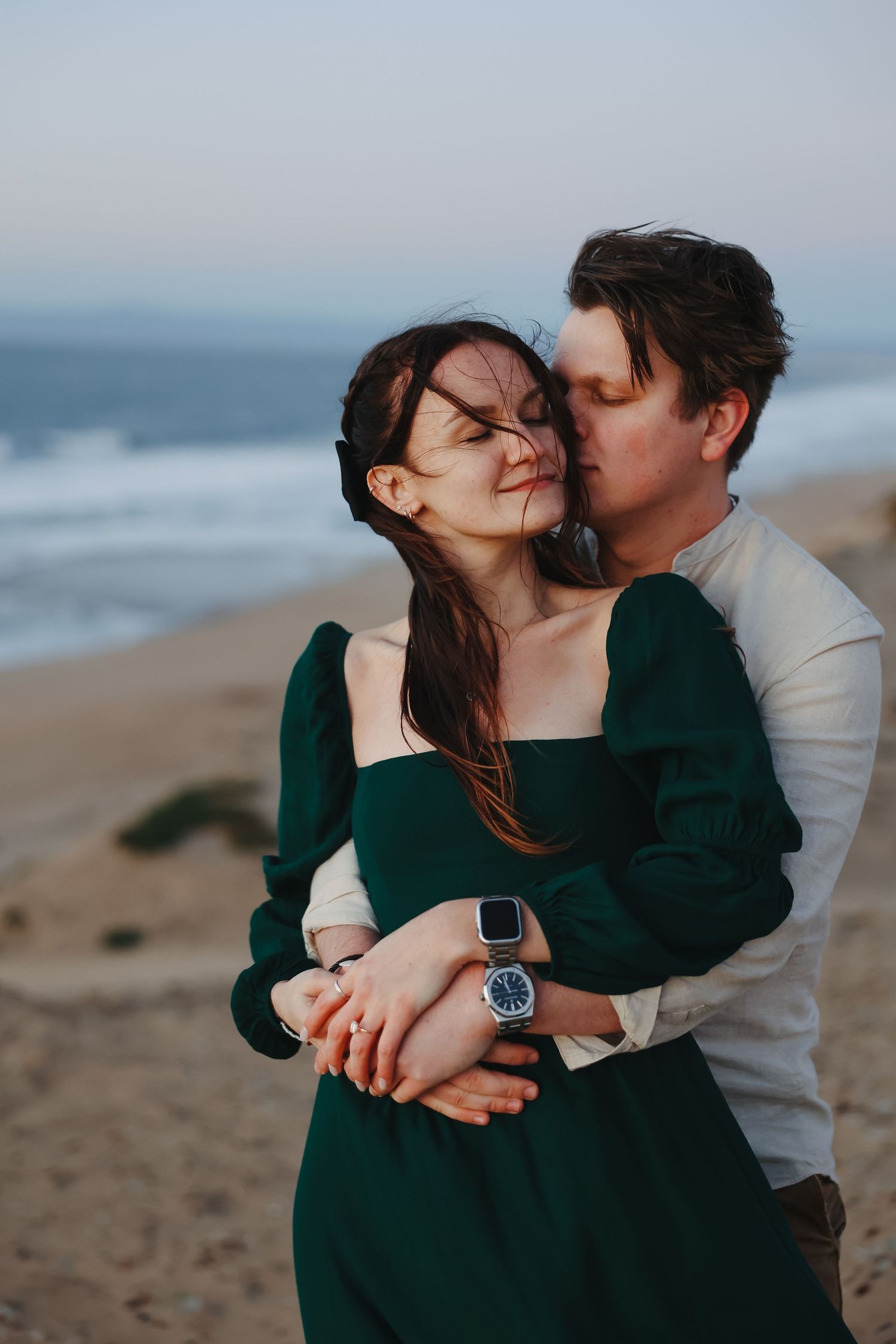 A romantic beachside moment as a couple embraces at sunset, with her wearing an elegant emerald green dress.