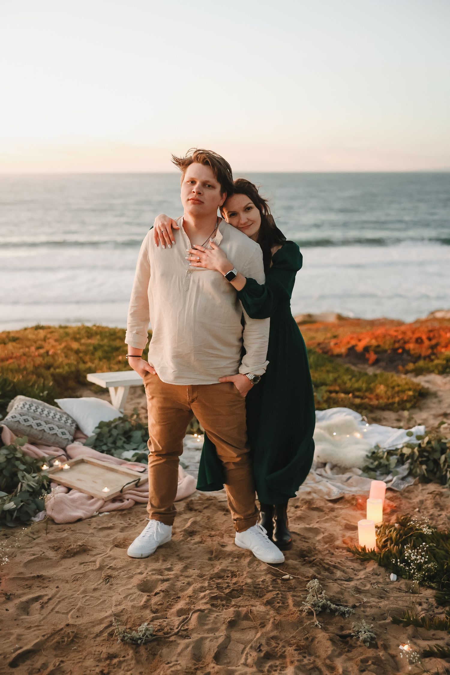 Tender embrace during sunset photoshoot on coastal cliffs with candlelit setting.