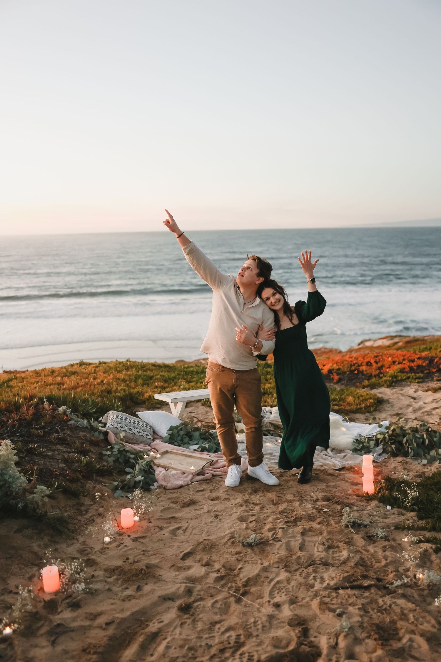 Playful poses and raised arms during sunset beach photoshoot with lit candles.
