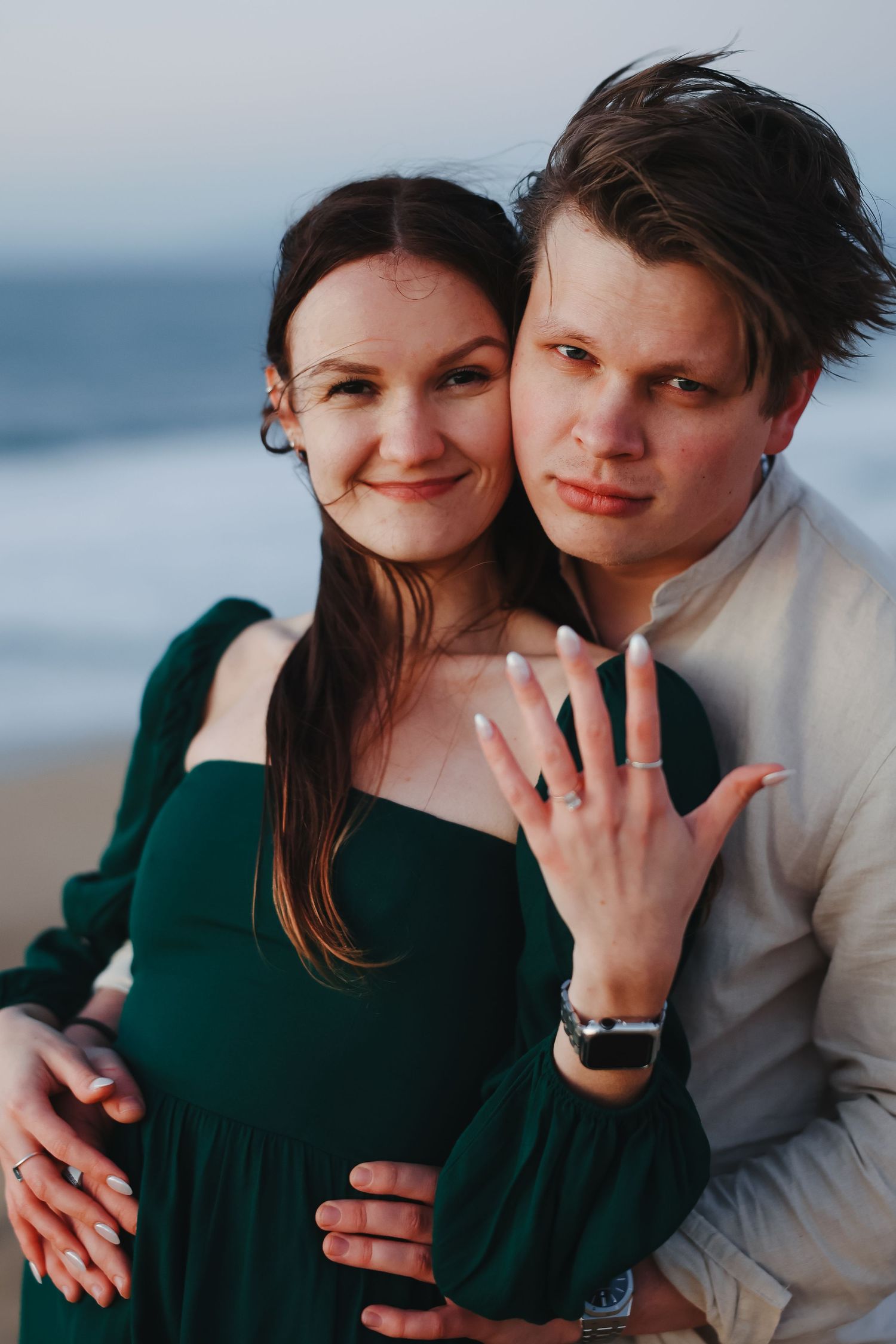 Happy couple shows off engagement ring in a casual beach photoshoot during golden hour.