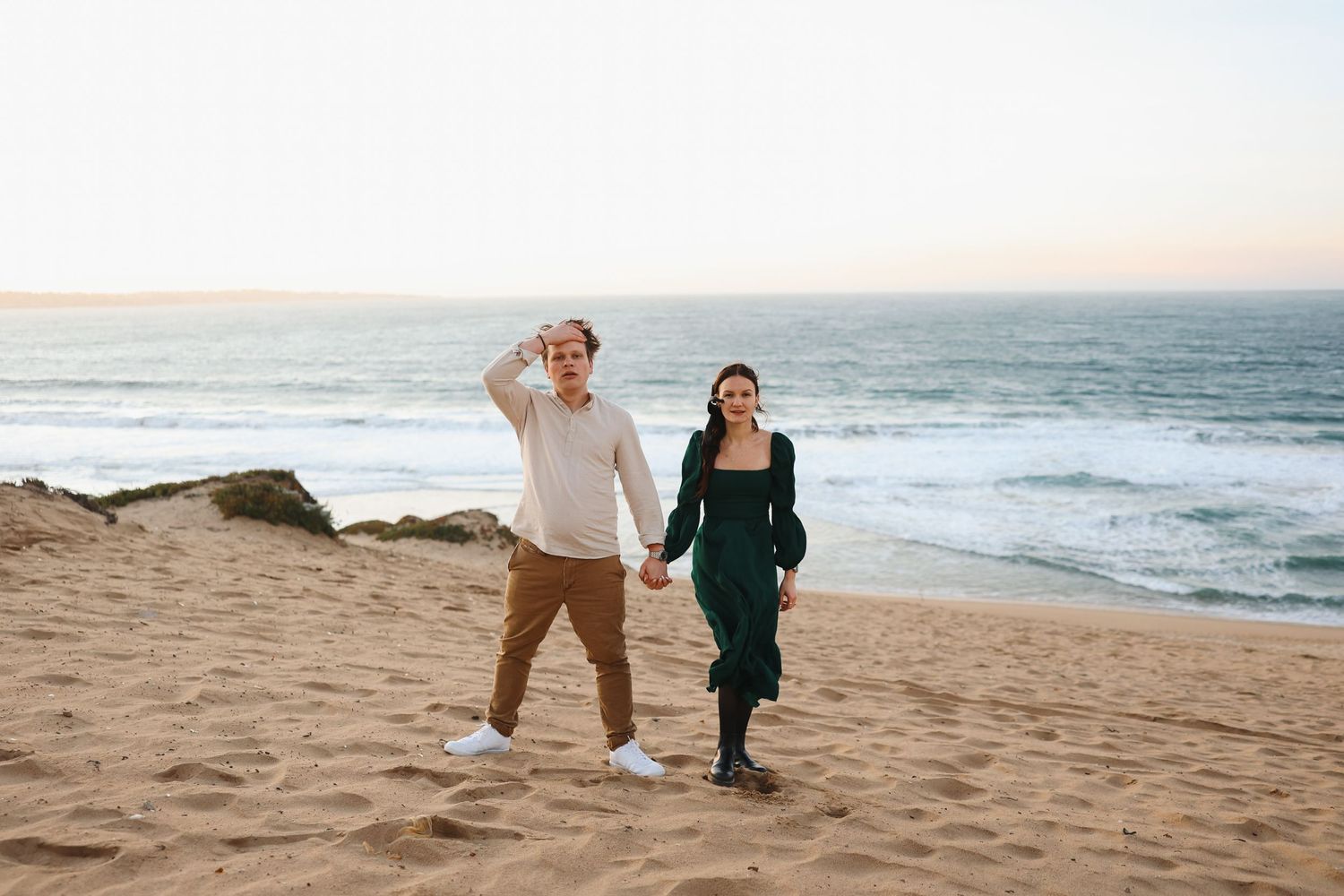 A joyful couple walks hand in hand along a scenic coastal beach at sunset.