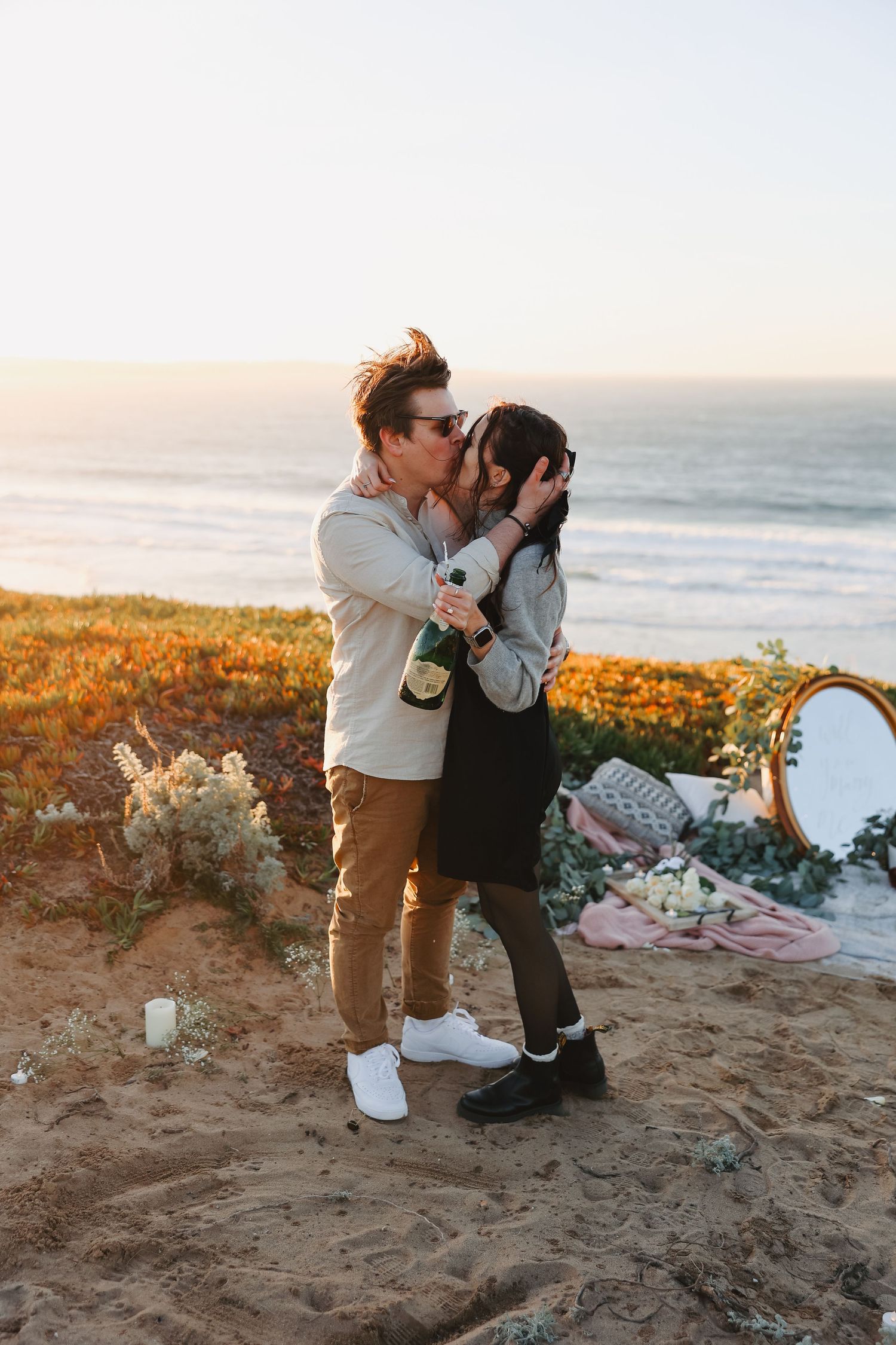 Romantic couple sharing an intimate moment on a scenic cliff overlooking the ocean at golden hour.