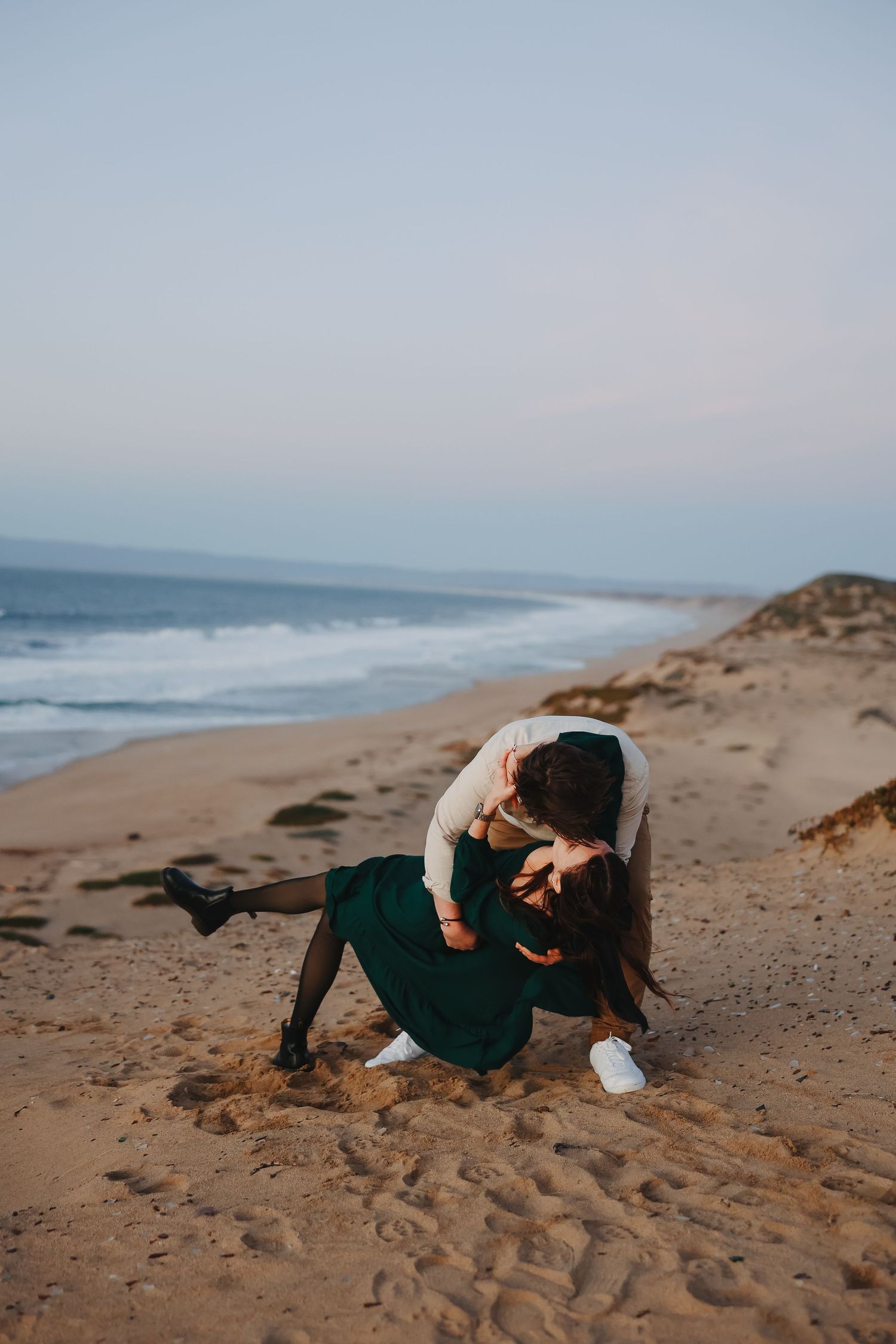 A couple shares an intimate moment while dancing on a scenic beach at sunset.