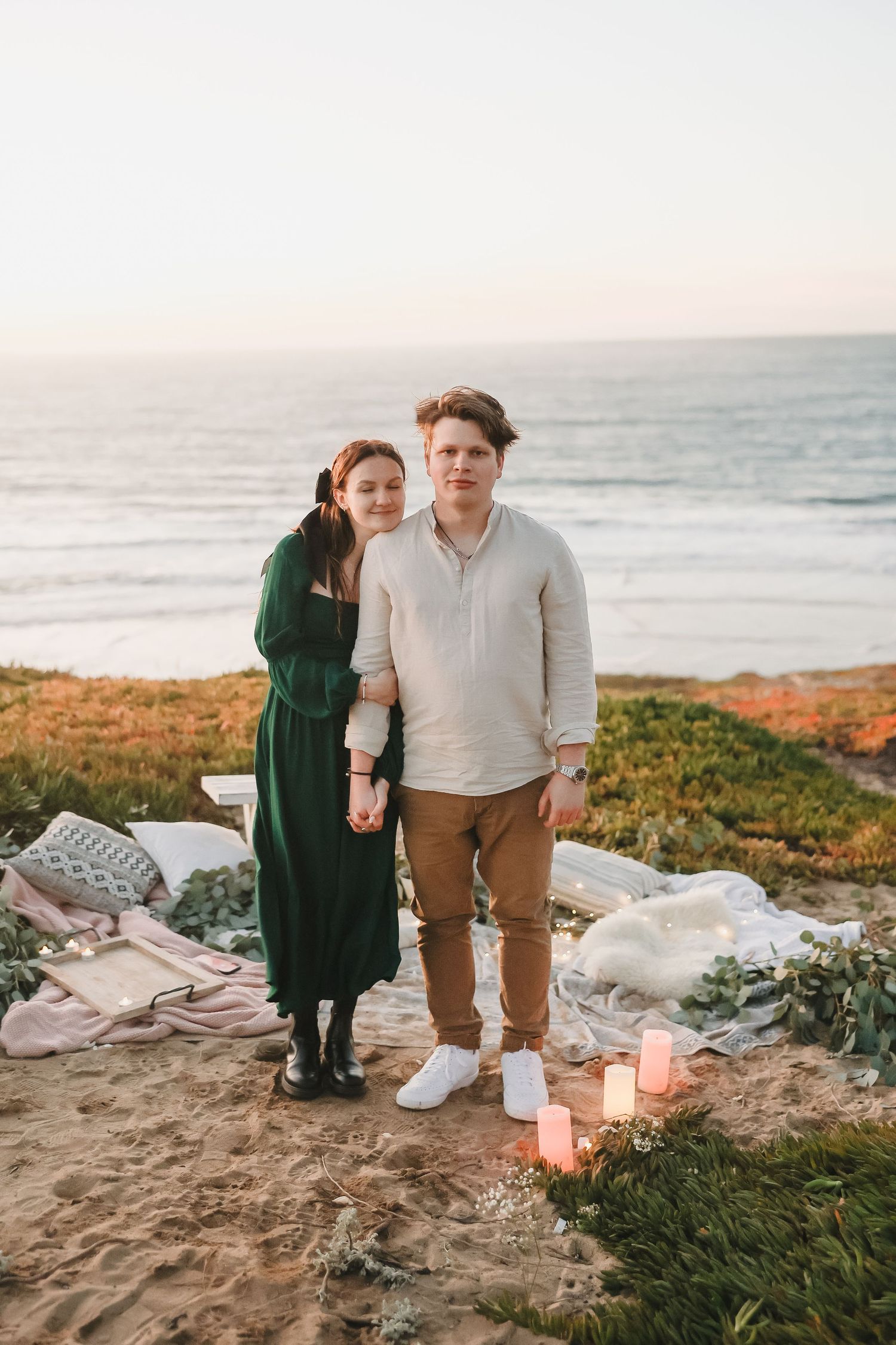 Candlelit evening picnic setup on oceanside cliffs with white blankets and romantic atmosphere.