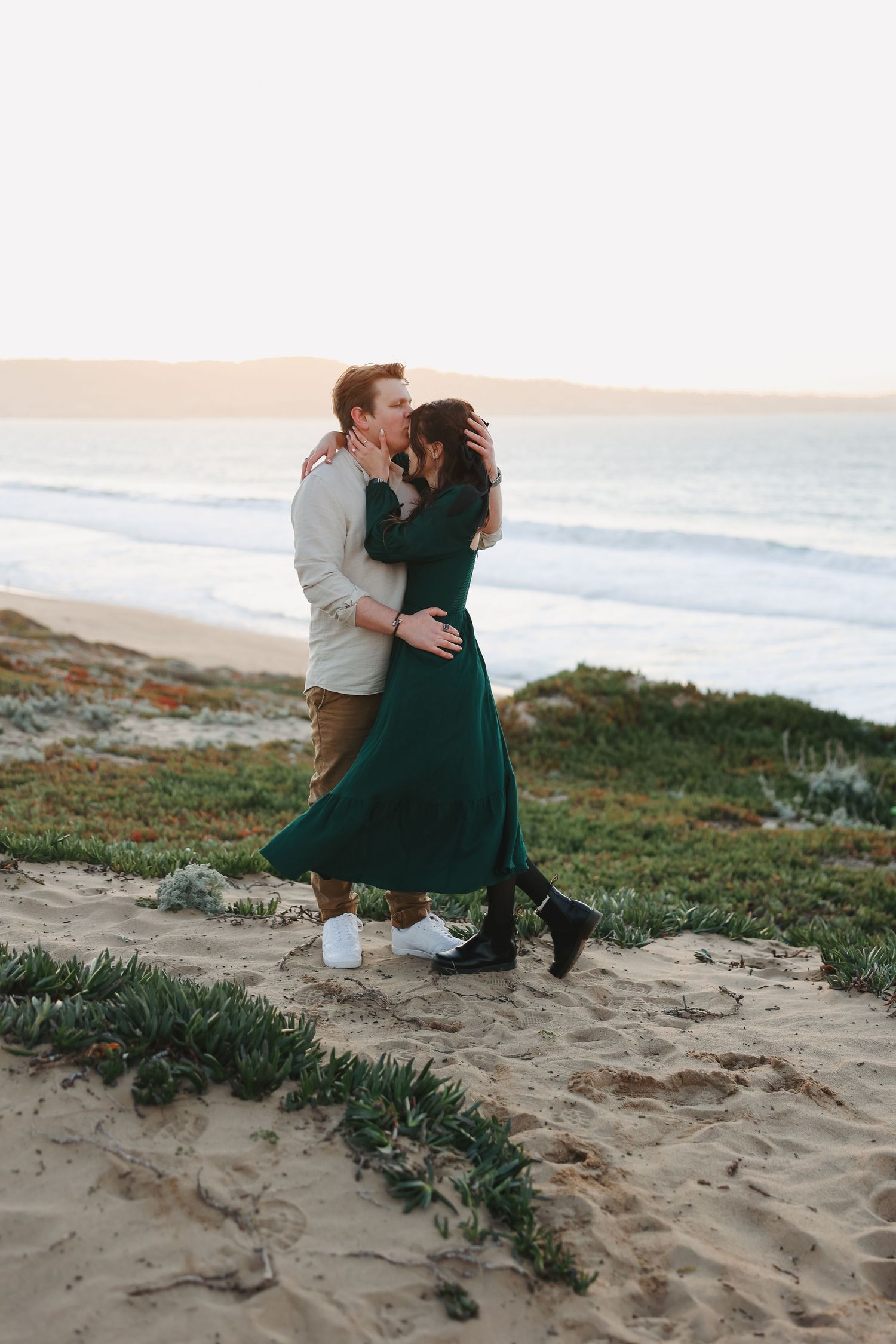 A romantic couple embraces on a sandy beach path at dusk.