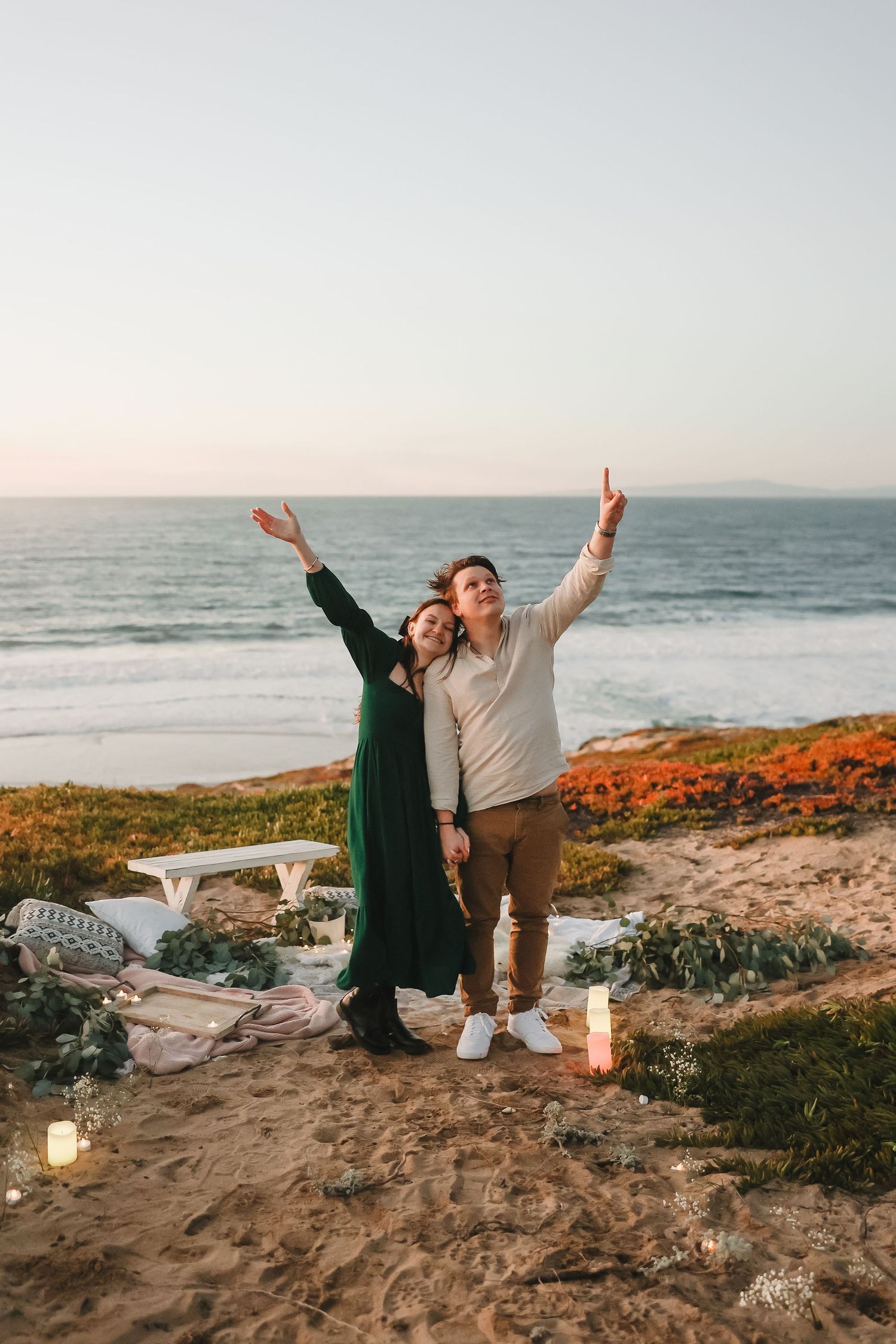 Joyful celebration pose against a scenic ocean backdrop with candles at sunset.