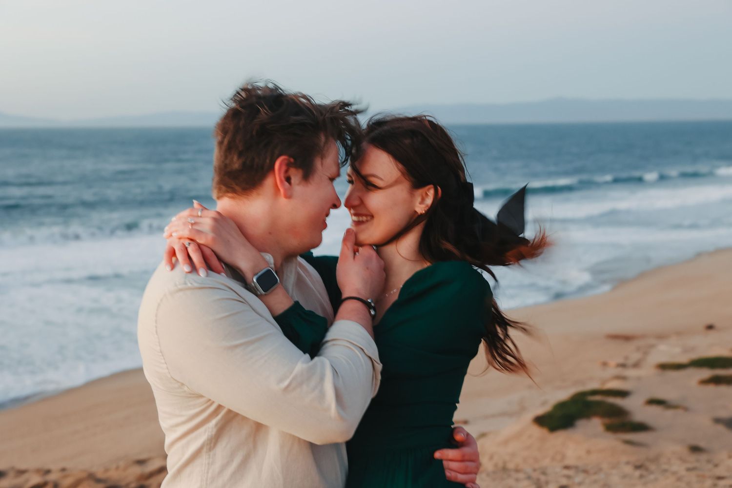 An intimate beachside portrait showing two people in a tender embrace with crashing waves behind them.