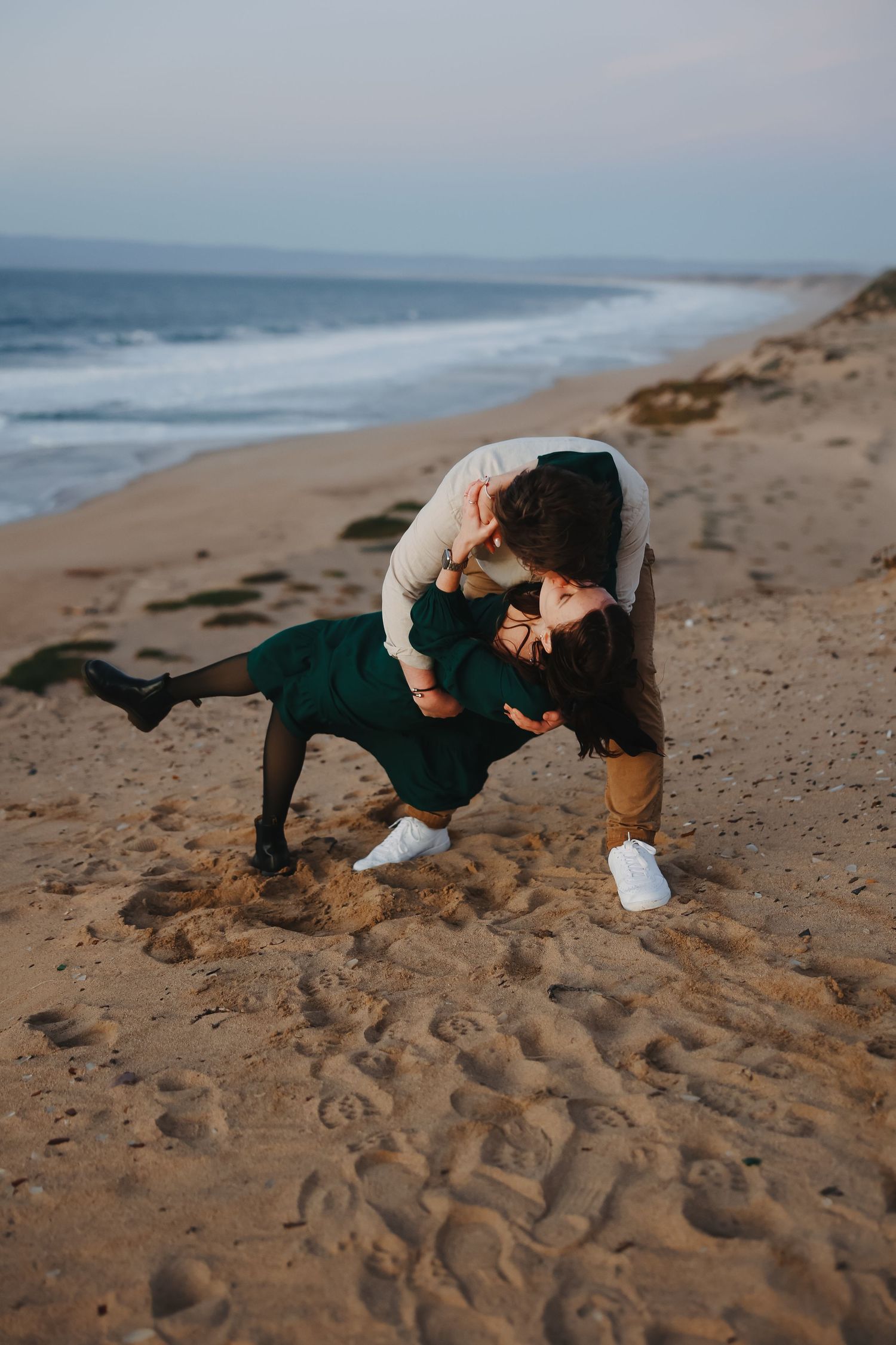 A couple dances intimately on a beach with ocean waves visible in the distance.