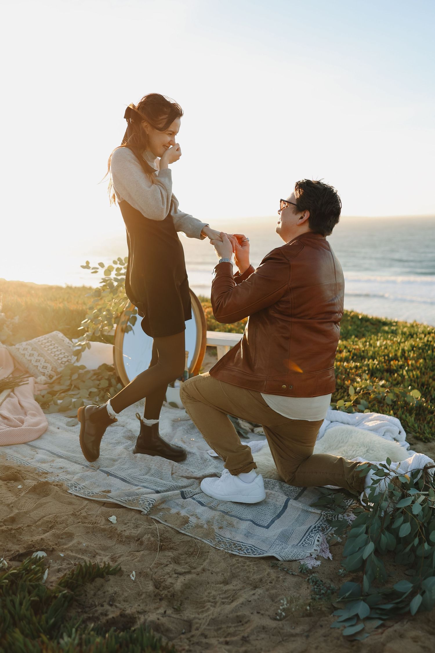 A sunset proposal scene on a cliff overlooking the ocean with a decorated picnic setup.
